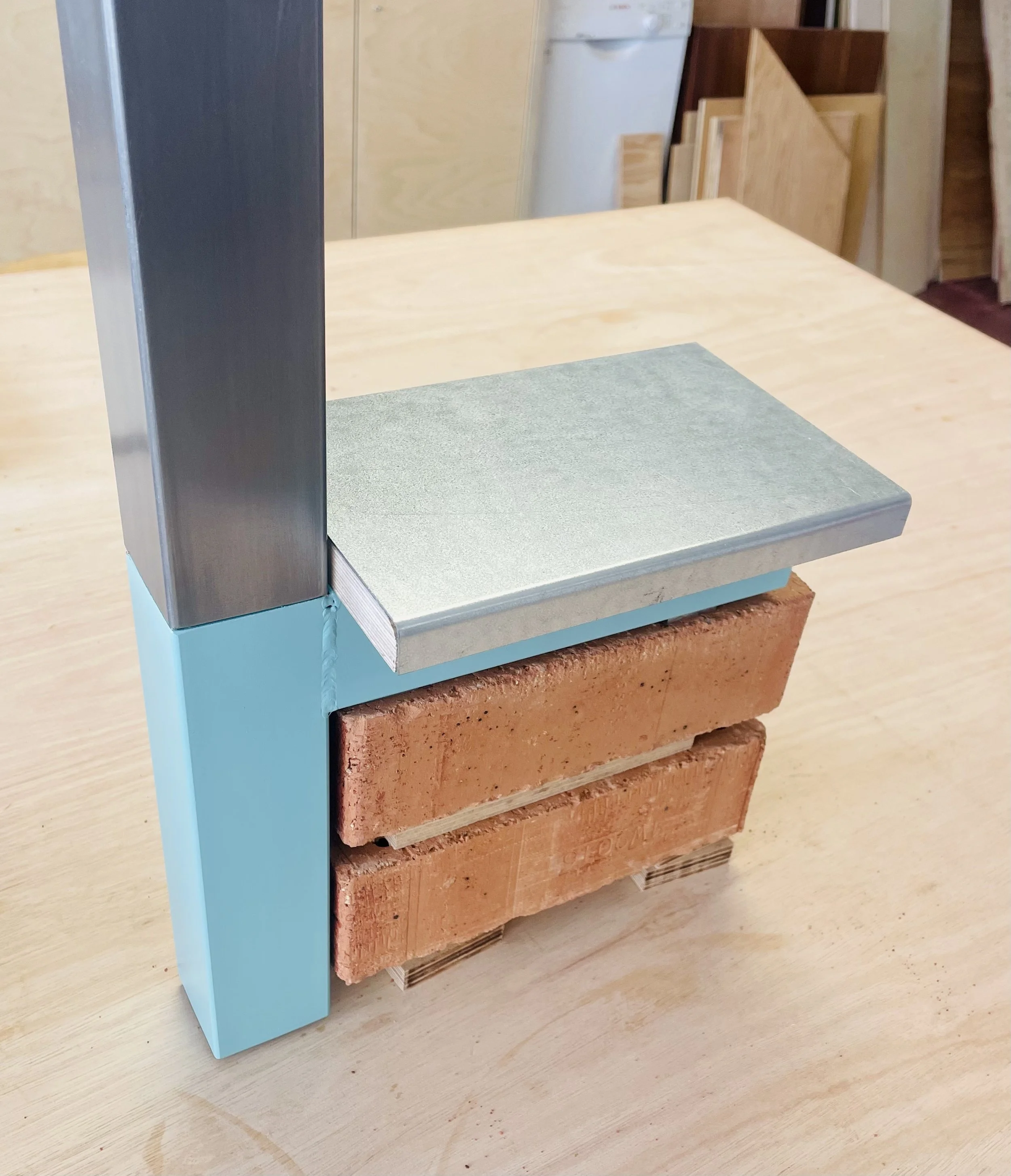 Close-up view of a construction model or display showing different types of materials and textures, including a blue foam block, a concrete slab, and stacked bricks, on a wooden surface.