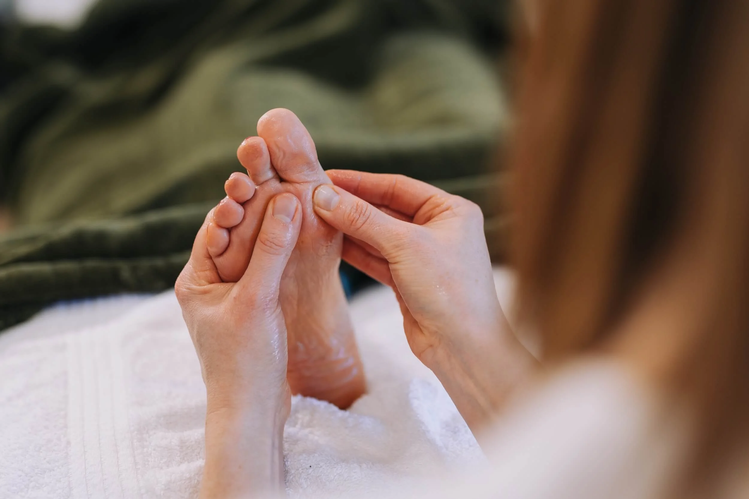 Close-up of a person's hands performing reflexology on another person's foot, with a soft, white towel underneath