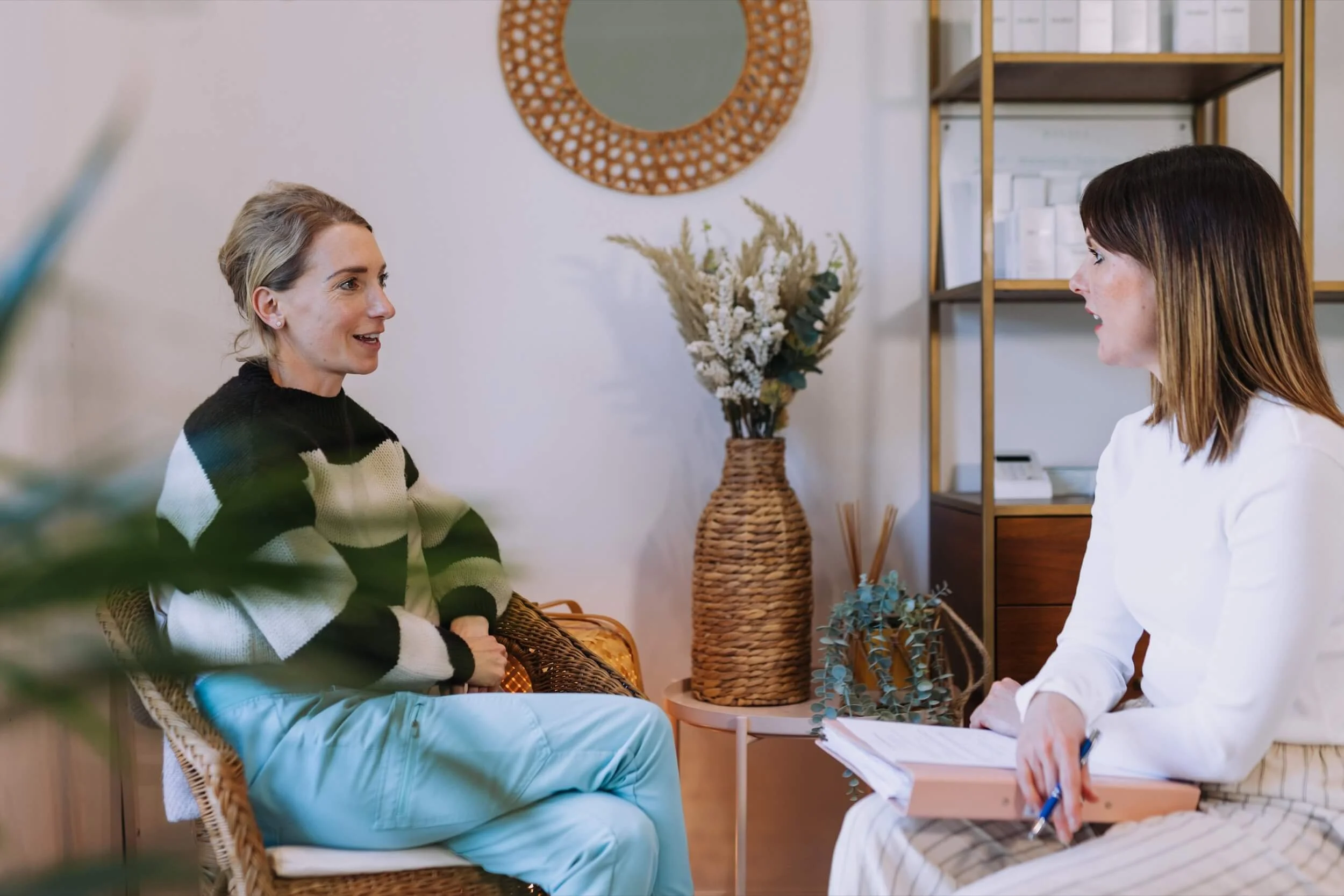 Two women having a conversation in a cosy and tranquil treatment room, decorated with plants and mirrors