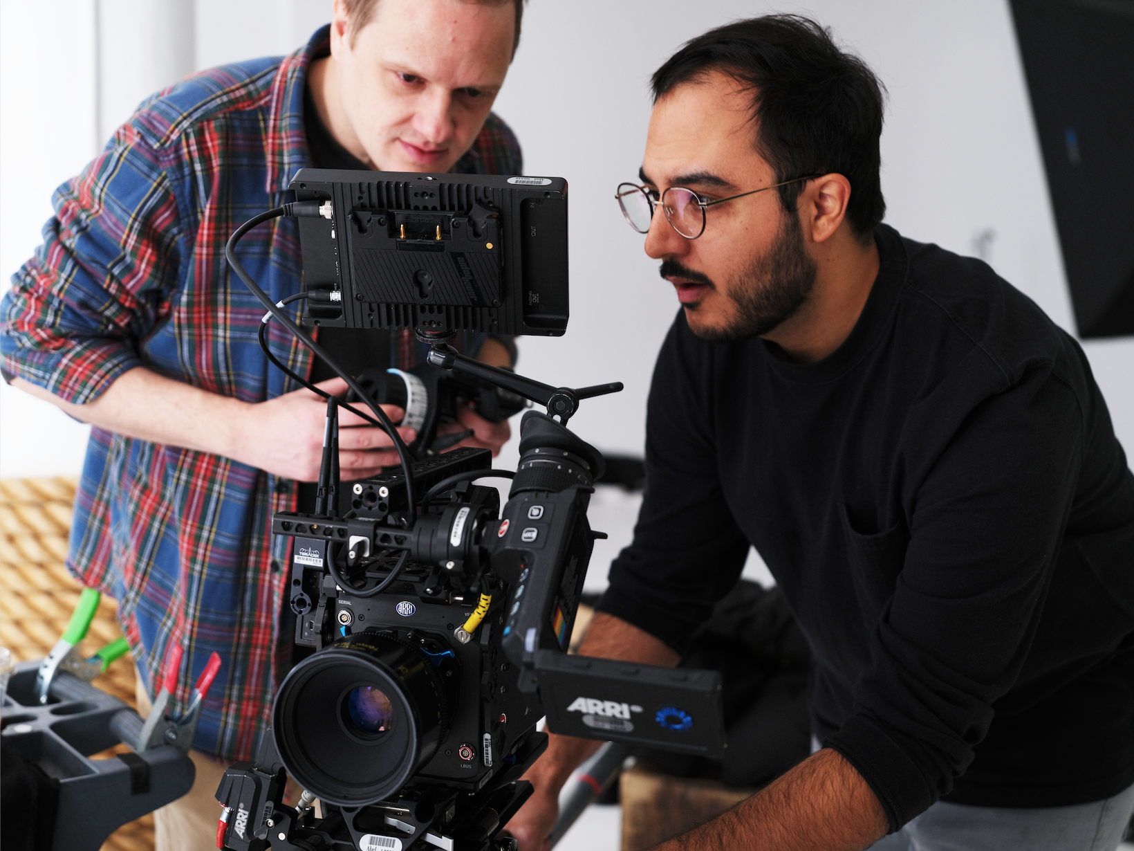 Two men working on filming equipment. One man is in focus, looking intently at the camera rig, while the other man is in the background, adjusting the camera.