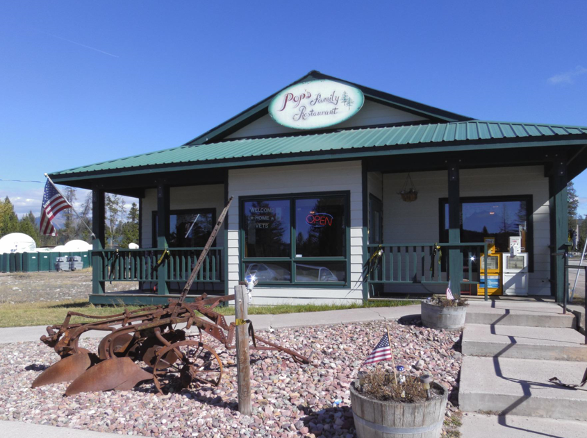 A small restaurant called 'Pop's Family Restaurant' with an American flag in front, an old rusty farming plow, a small American flag in a flowerpot, and a sidewalk with steps leading to the entrance, under a blue sky.