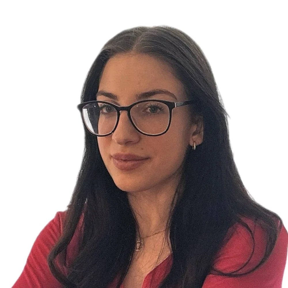 Portrait of a woman with long dark hair, wearing glasses and a red top, looking slightly to the side against a plain white background.