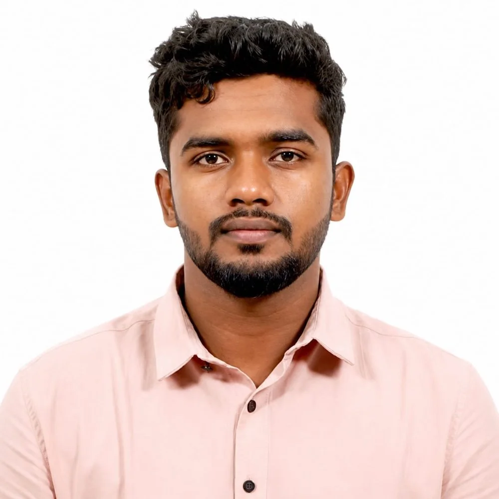 A portrait of a young man with dark hair, a beard, and wearing a light pink collared shirt, against a plain white background.