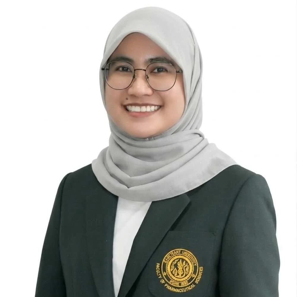 A woman wearing glasses, a hijab, and a professional black blazer with a badge that says 'UAE University of Pharmaceutical Sciences'.