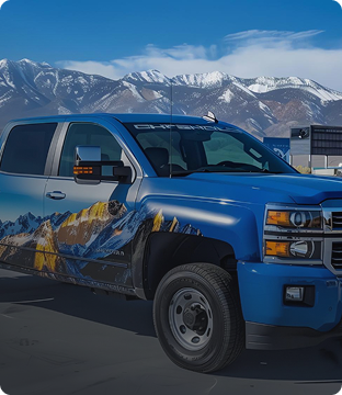 A blue pickup truck with mountain scenery and snow-capped peaks in the background.