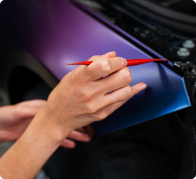 A person applying a vinyl wrap to a car's purple and blue surface.