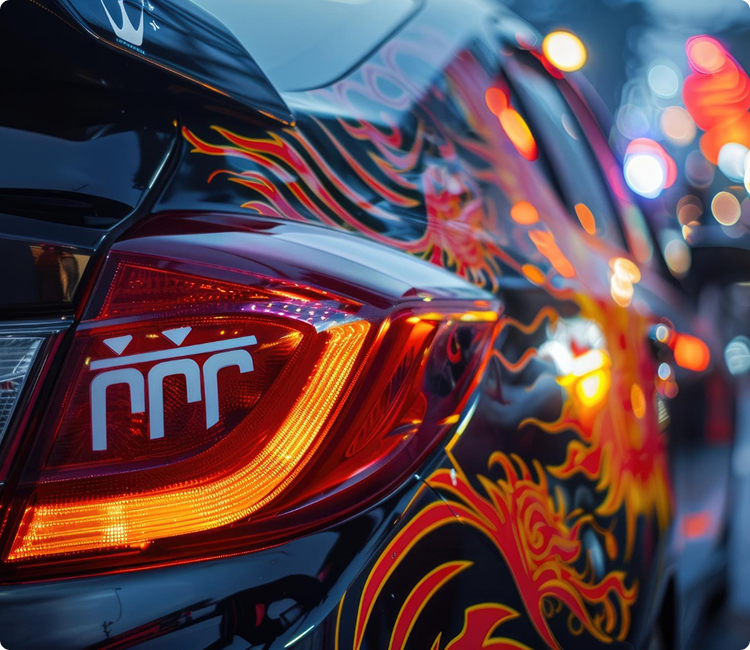 Close-up of a car with a vibrant, flame-themed decal design and illuminated taillight at night, with city lights in the background.