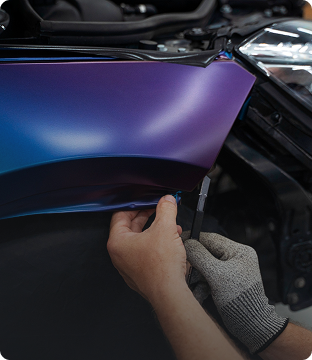 Person installing a purple and blue vinyl wrap on a car's hood.