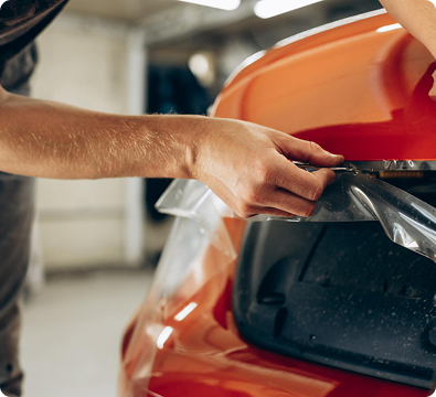Person working on the hood of a red car in a garage.