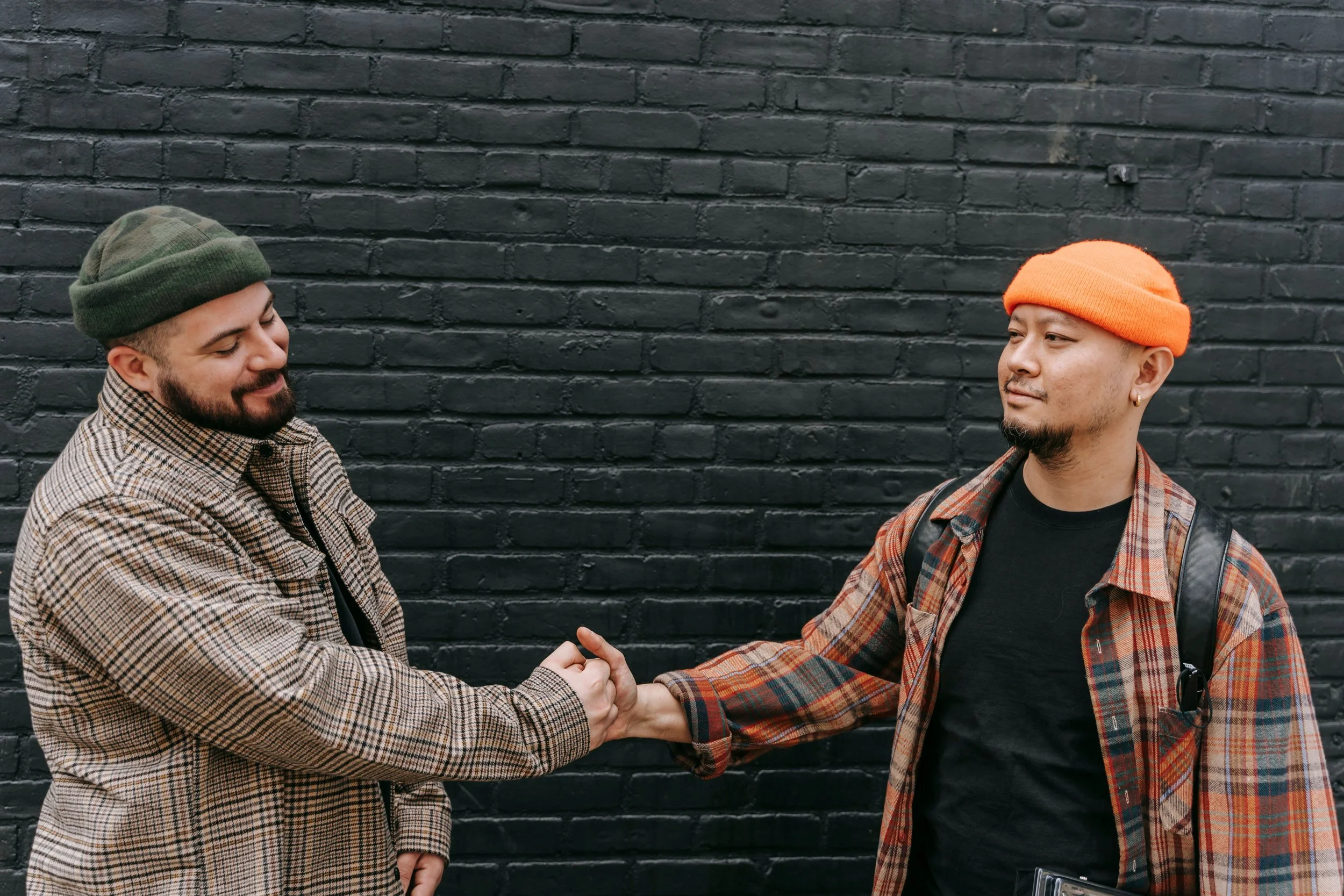Two men warmly shaking hands outdoors, symbolizing relational connection, siblinghood, and mutual support.