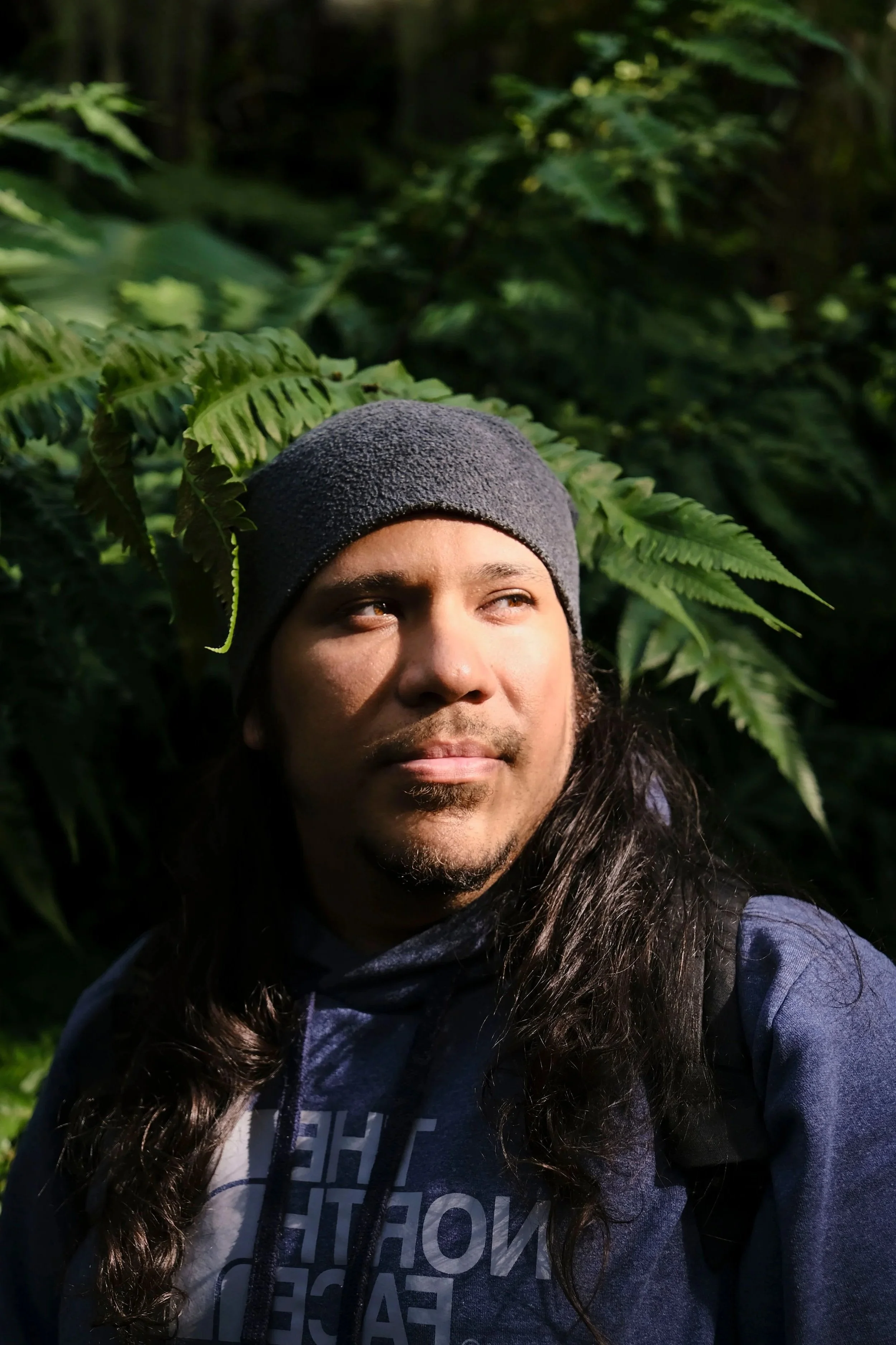 Man standing mindfully under lush green fern leaves, representing somatic grounding and nature connection.
