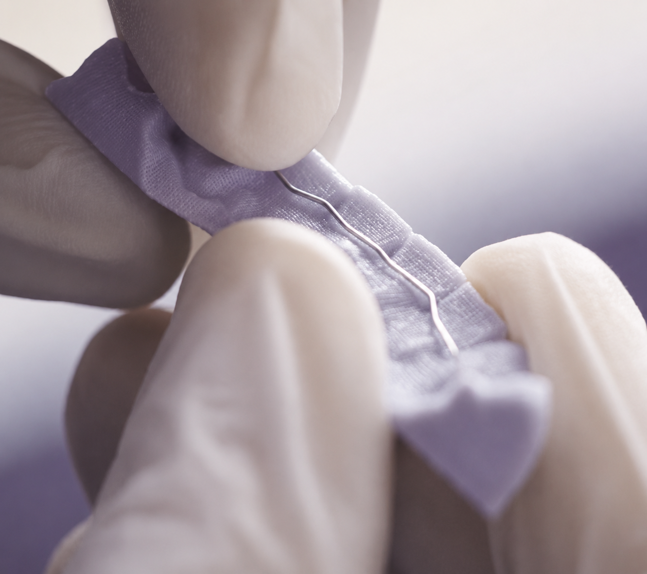 Close-up of a dentist or dental technician using a dental tool on a small section of a dental model or prosthetic with a purple fabric or cloth on the surface.