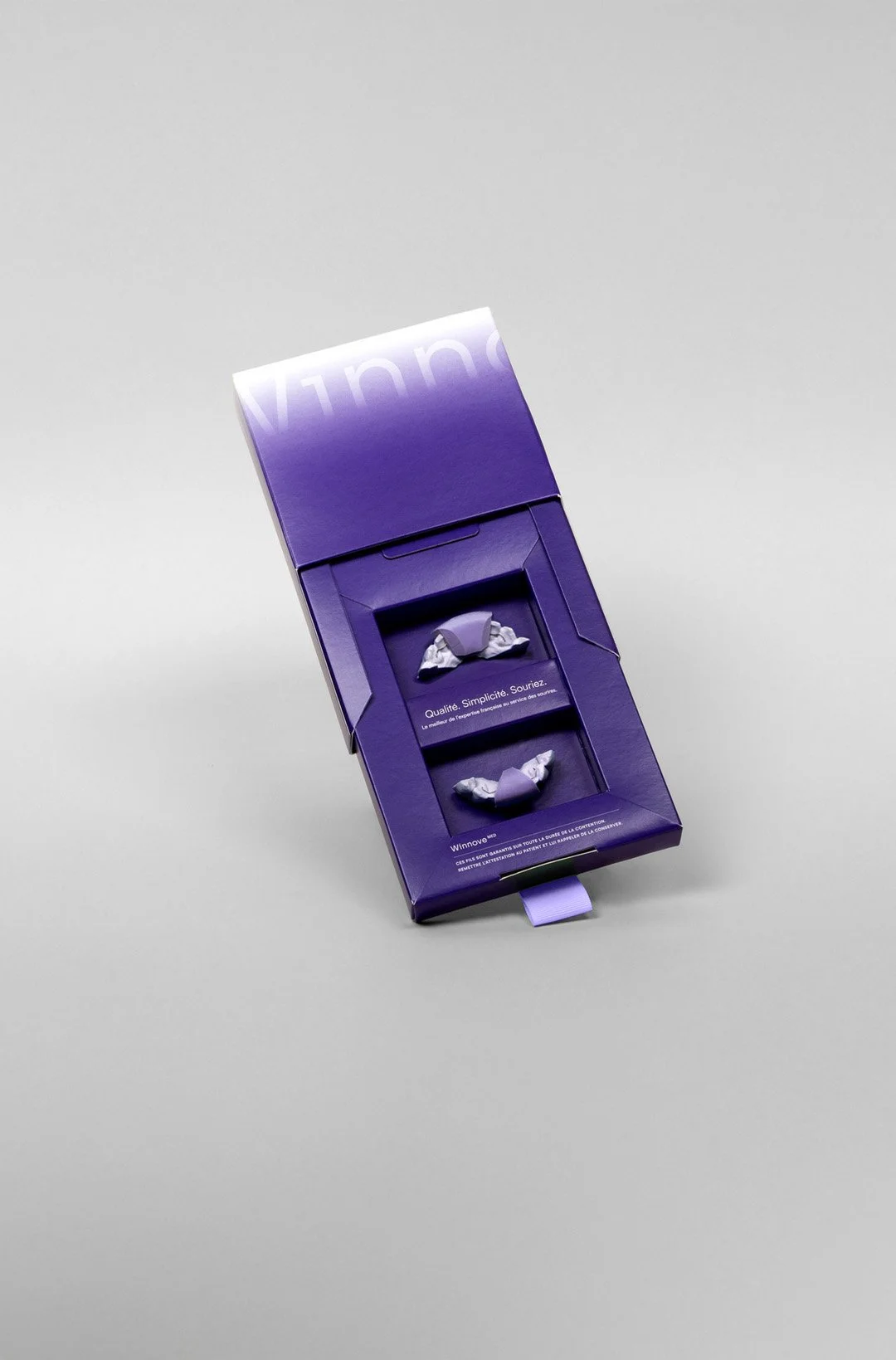A purple box with tissues inside, displaying in French the words 'Qualité, Simplicité, Souriez.'
