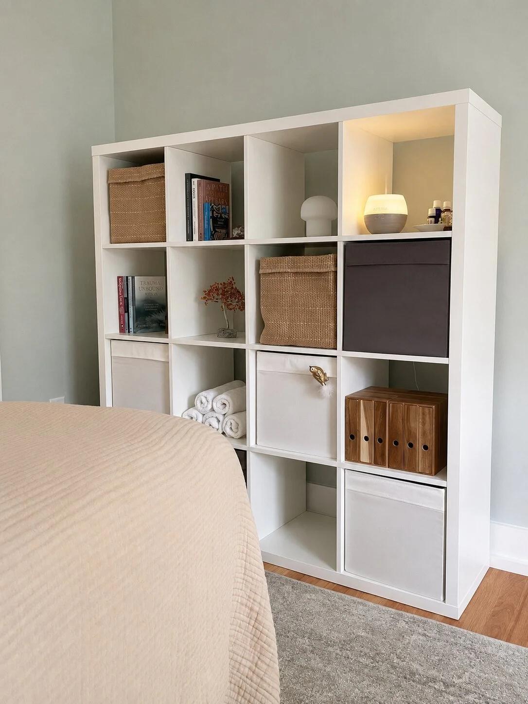 Organized massage studio shelves with linens, books, baskets, and warm lighting.