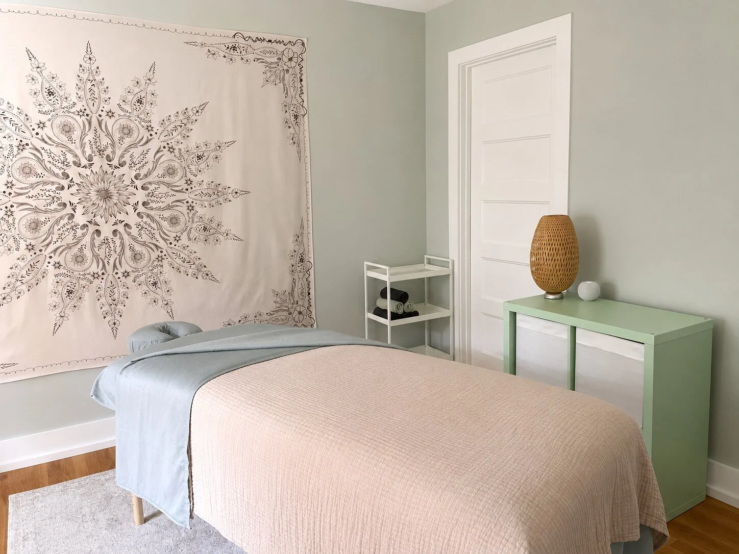 Massage table in a calm treatment room with a botanical wall hanging and soft green decor.