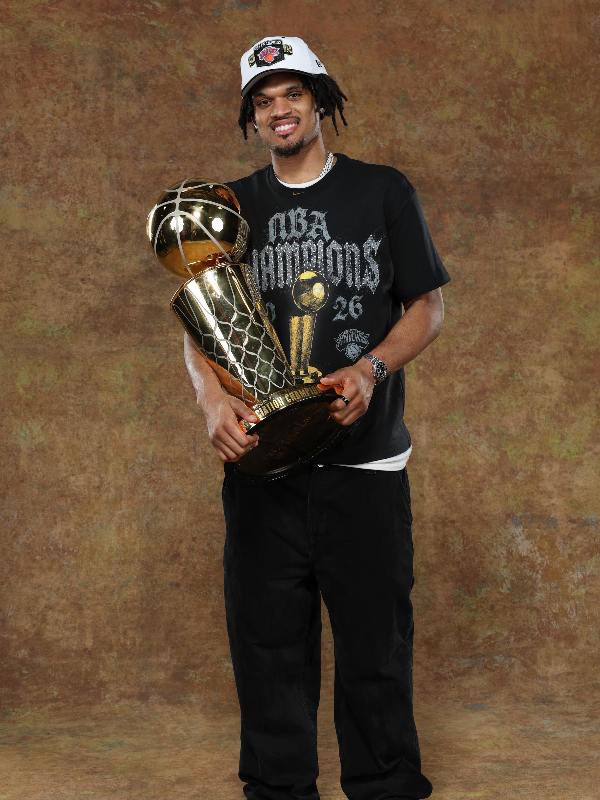 Dillon Jones wearing a baseball cap, black T-shirt, and watch, holding a shiny basketball trophy and smiling.