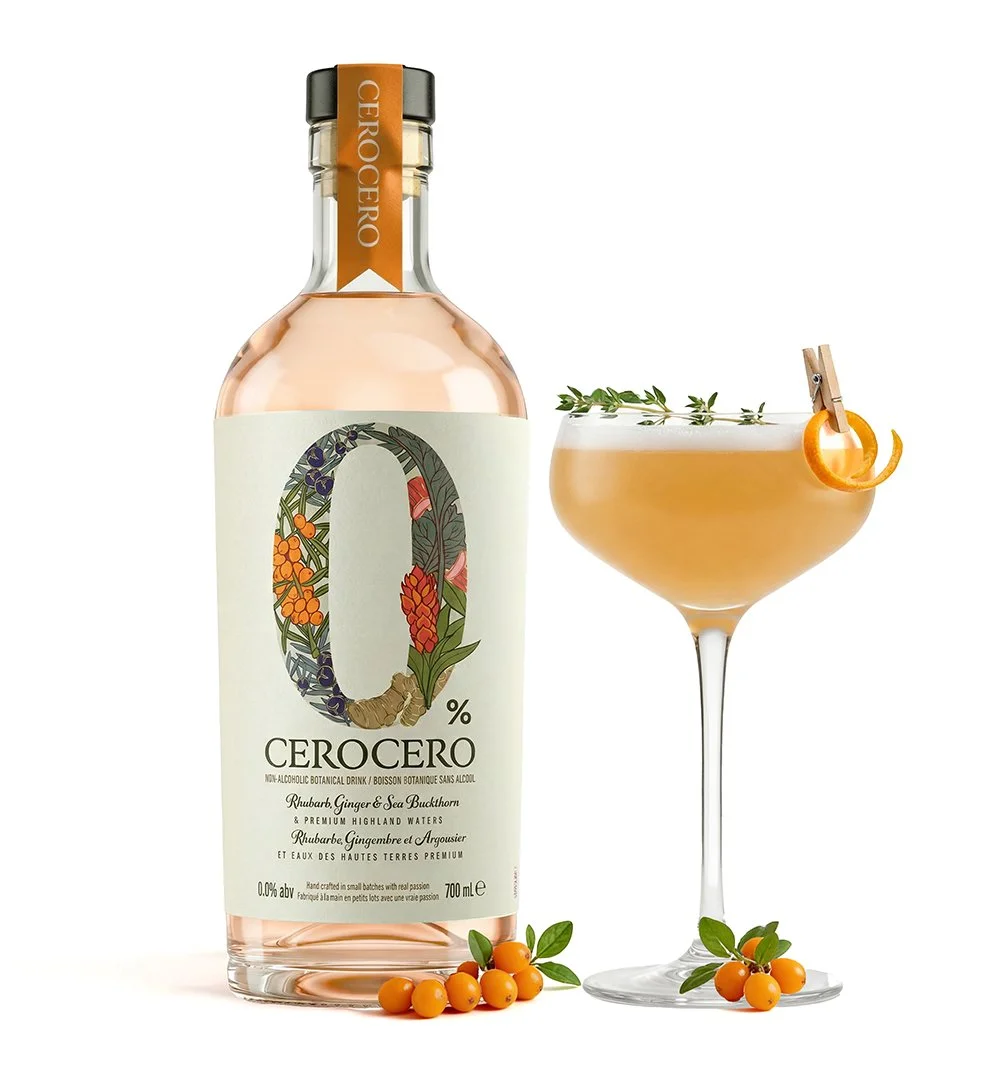A bottle of Cerocero non-alcoholic botanical drink with rhubarb, ginger, sea buckthorn, rhubarb, ginger, and argousier flavor, placed next to a cocktail glass filled with a pinkish drink garnished with a twist of orange peel, a sprig of herbs, and sm