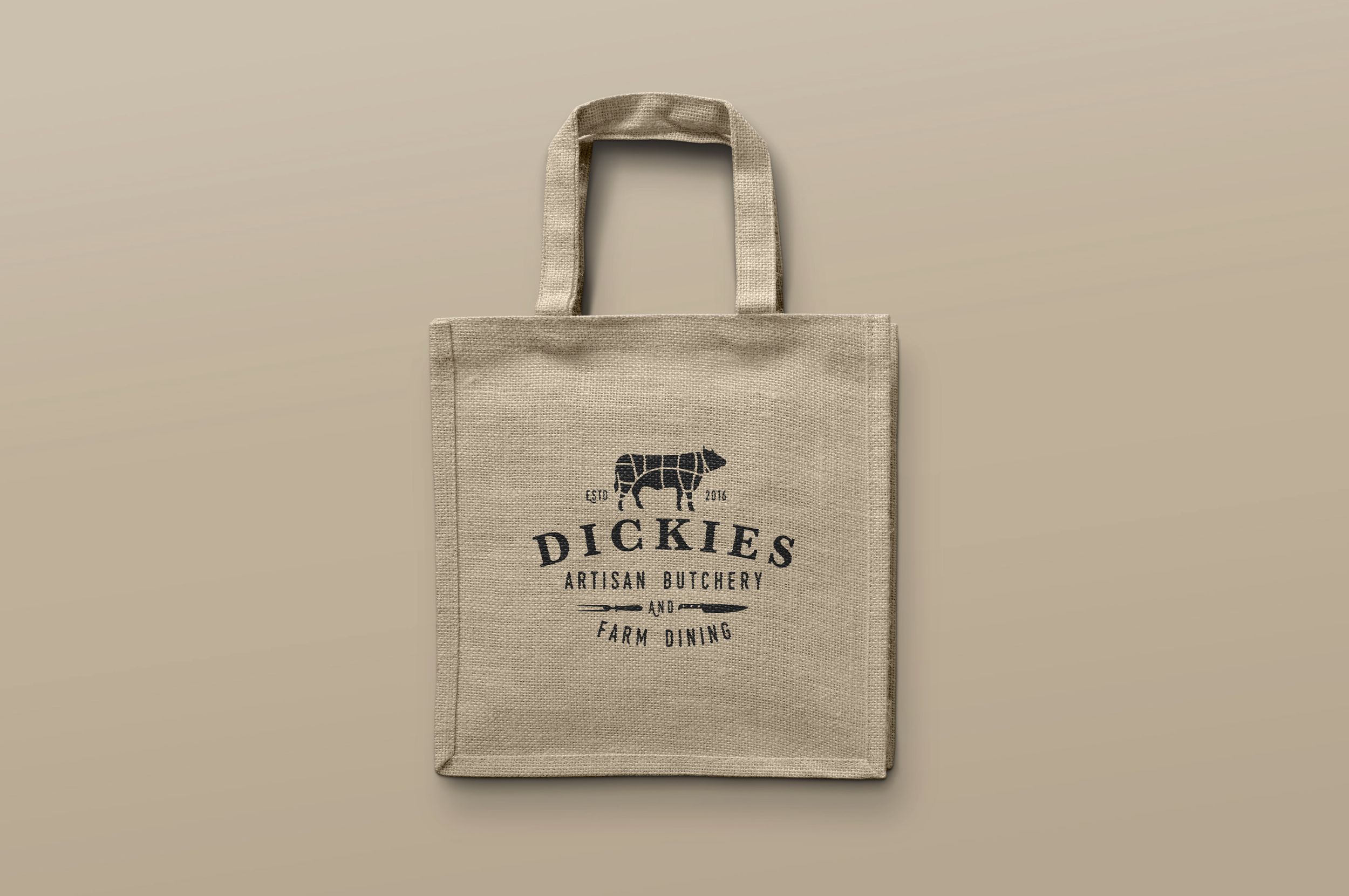 Beige fabric tote bag with black text and logo for Dickie's Artisan Butchery and Farm Dining, hanging against a beige background.