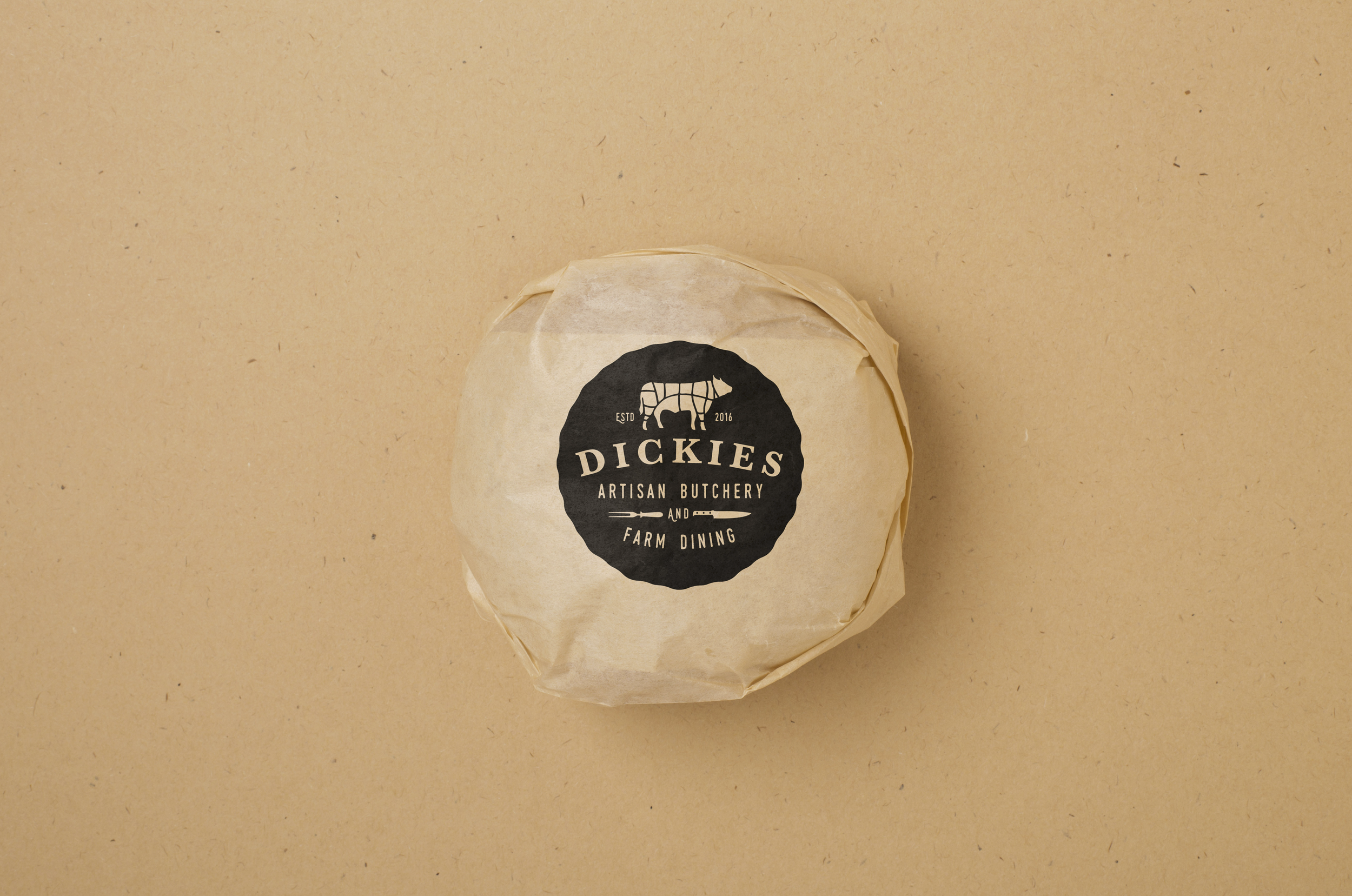 A paper wrapped package with a black logo reading "Dickies Artisan Butchery and Farm Dining" on a light brown background.