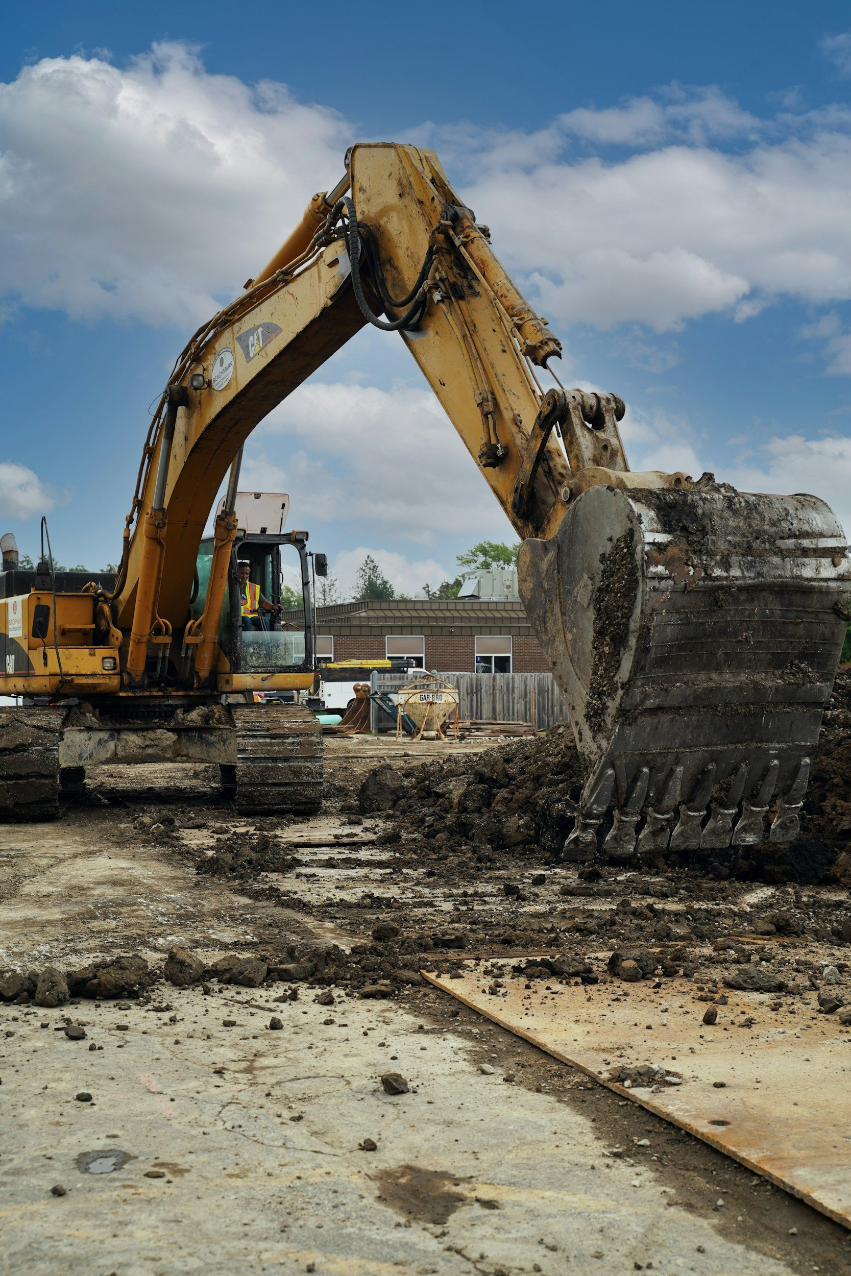 A yellow excavator digging up the ground on a construction site under a partly cloudy sky.