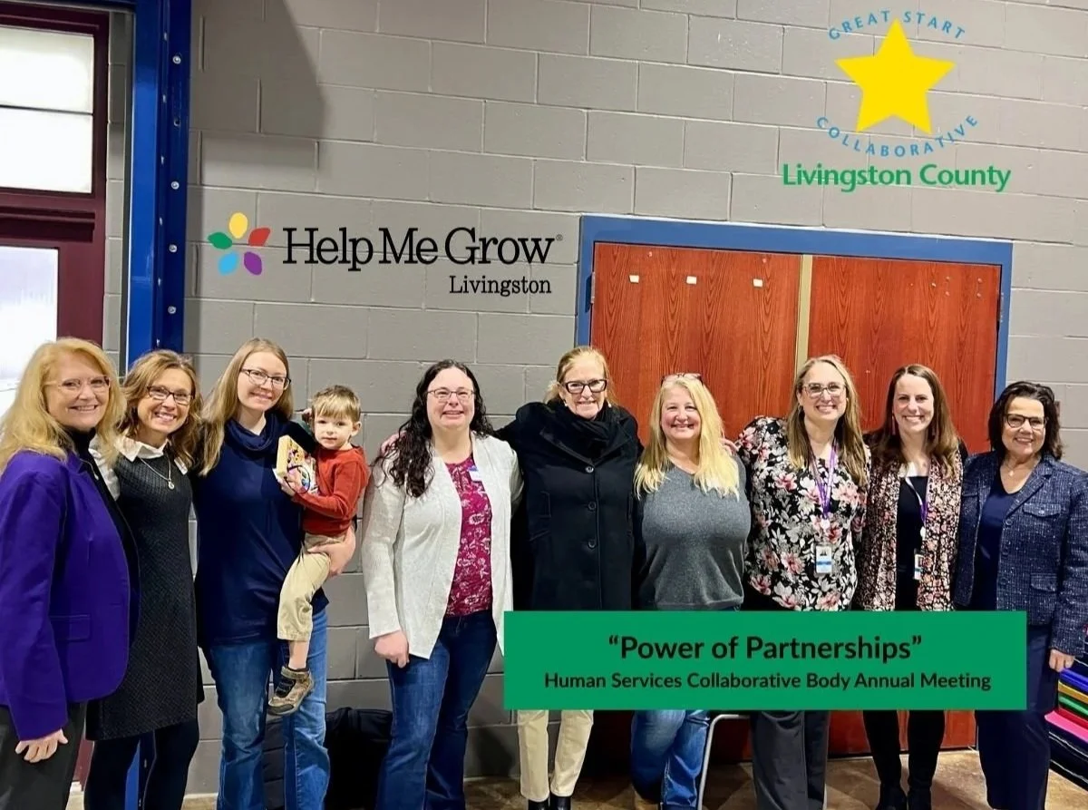 Group of nine women and one young boy standing in a line indoors, smiling, at a community event titled 'Power of Partnerships' for the Human Services Collaborative Body Annual Meeting in Livingston County. The background features a gray brick wall with signs including 'Help Me Grow Livingston' and a colorful star logo for 'Great Start Collaborative Livingston County'.