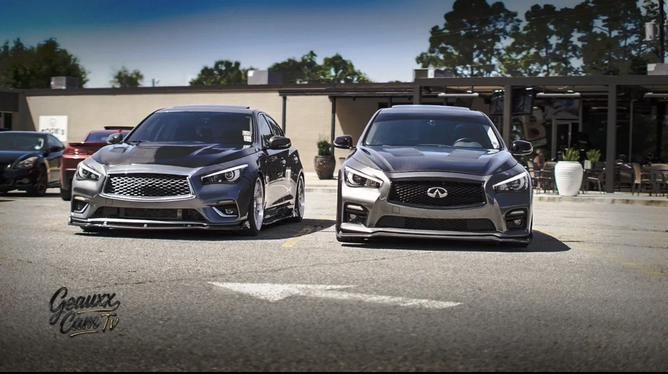Two gray sedans parked side by side in a parking lot outside a restaurant with outdoor seating and potted plants.