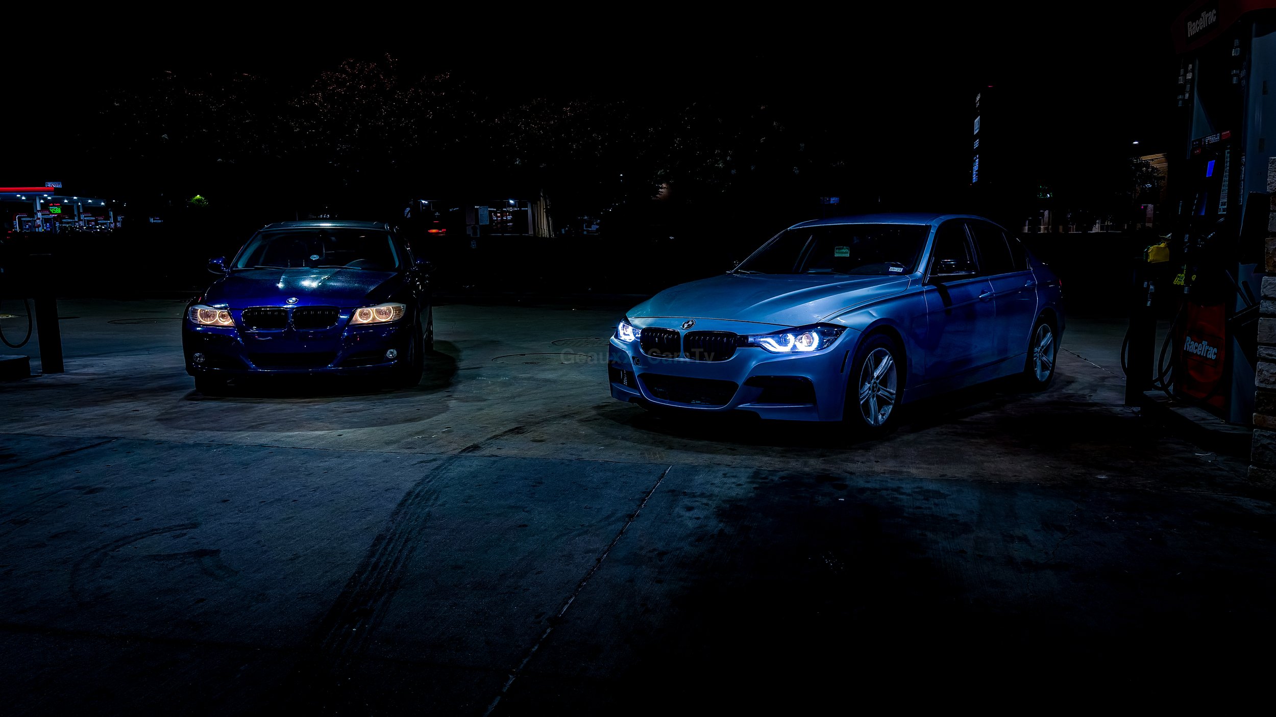 Two BMW cars parked at a gas station at night, illuminated by artificial lighting.