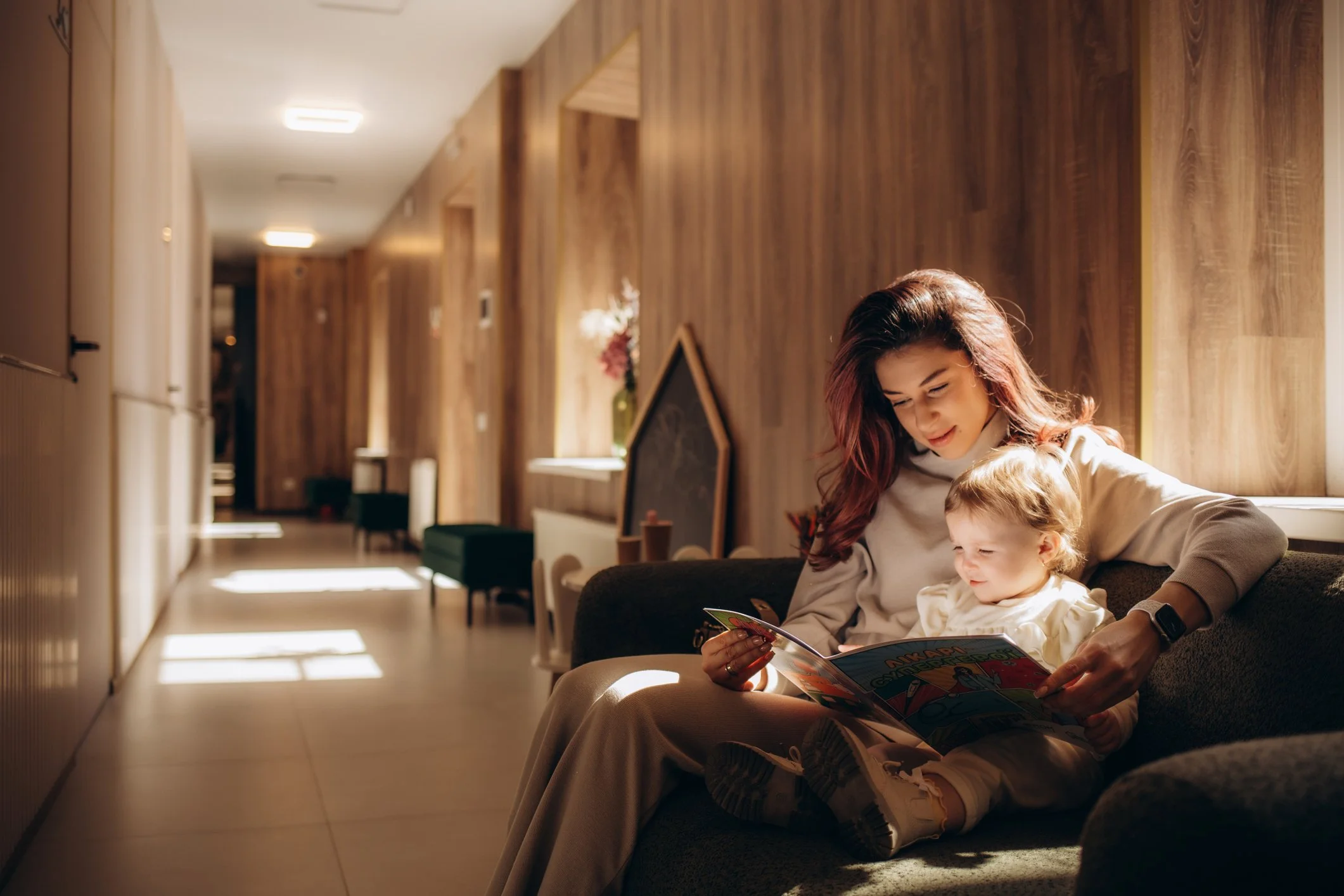 Caregiver and child reading together on a sofa in a warm, softly lit home.
