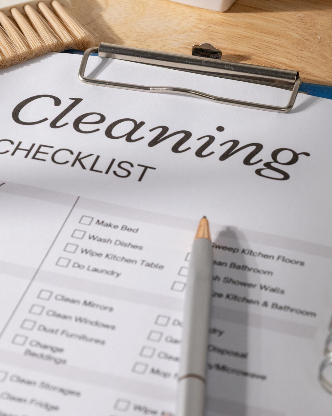 Clipboard with a cleaning checklist, a pen, a broom, and a container in the background.