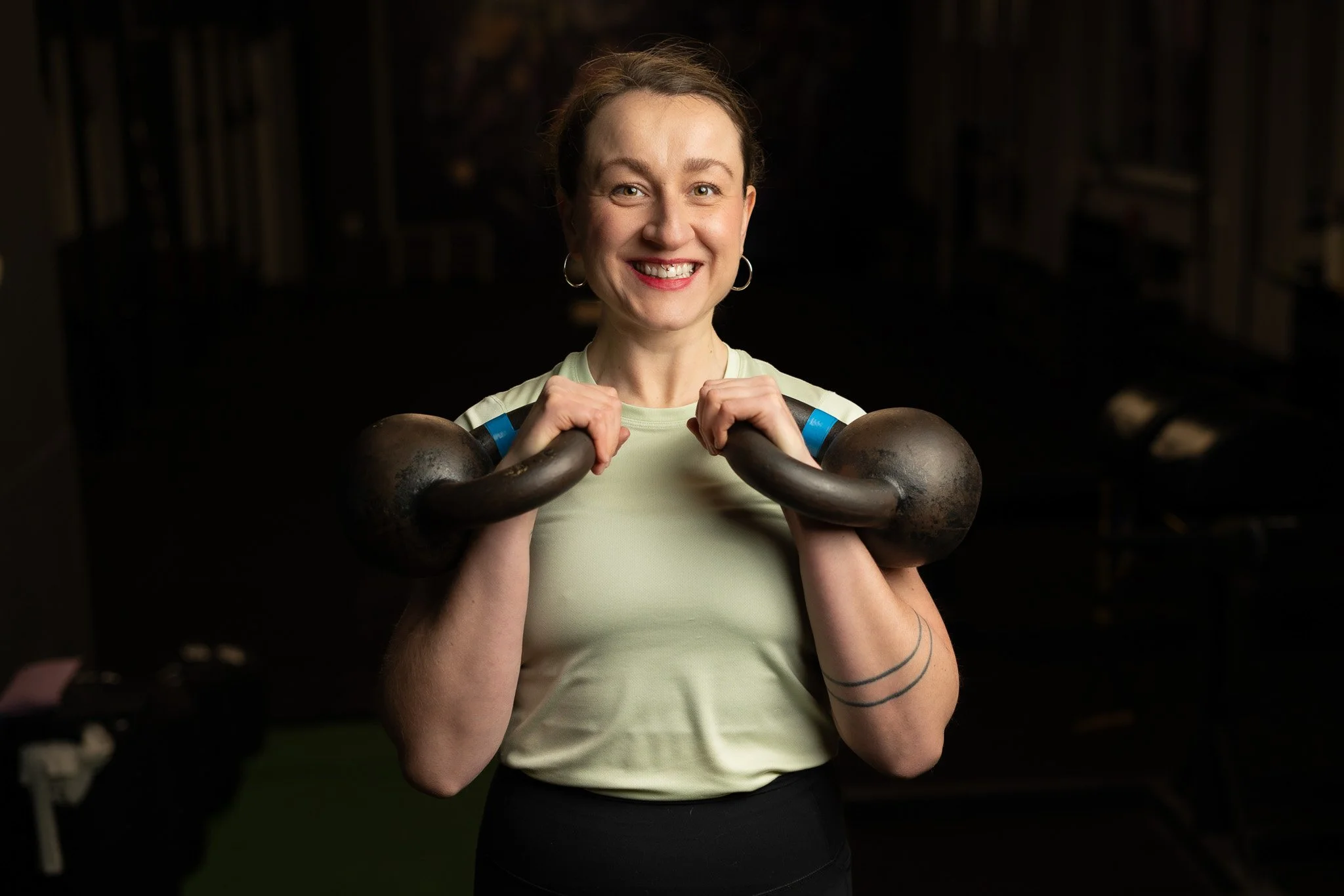 A smiling woman holding a kettlebell at the gym.