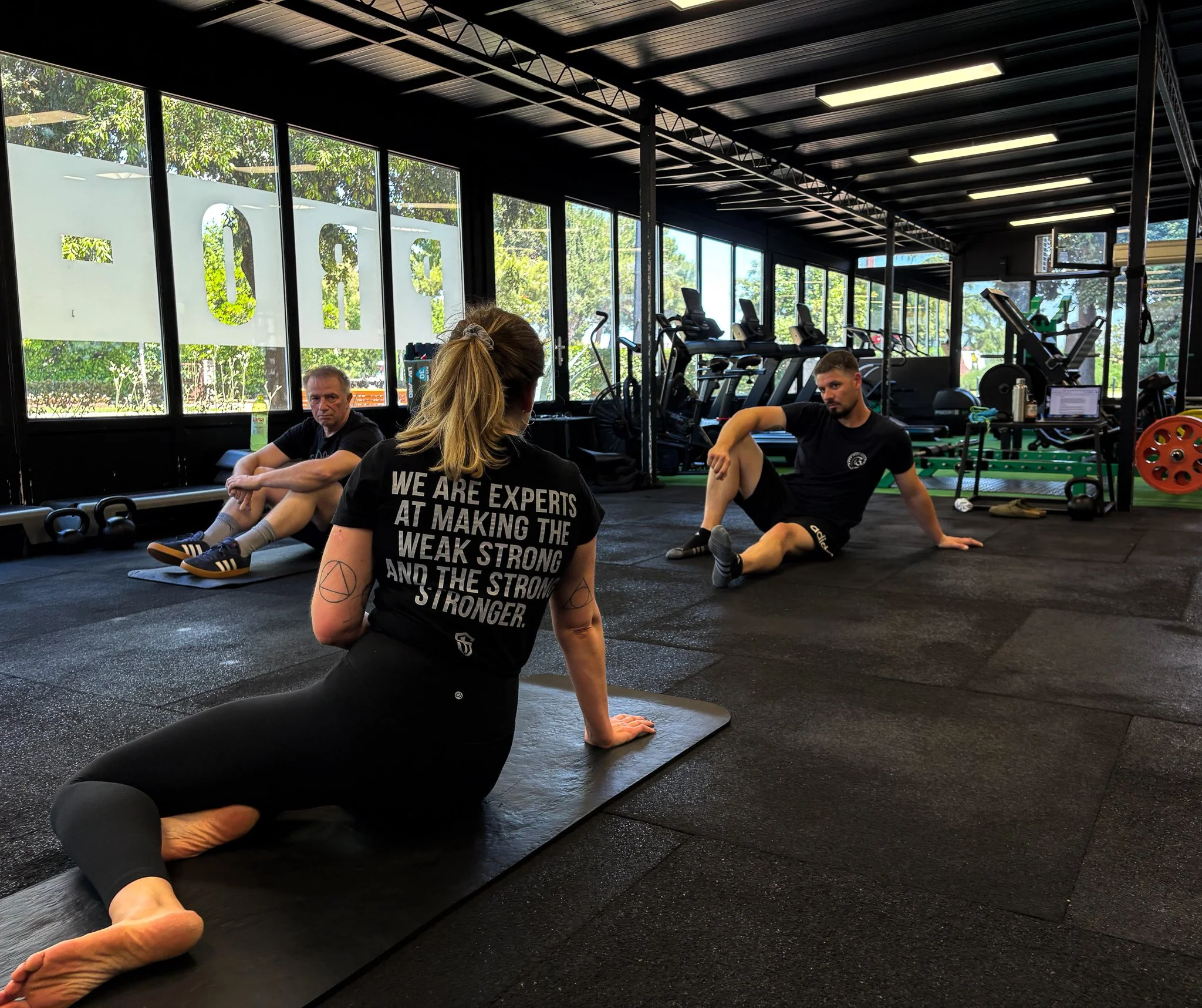 People in a gym exercising, with gym equipment like treadmills and weights in the background.