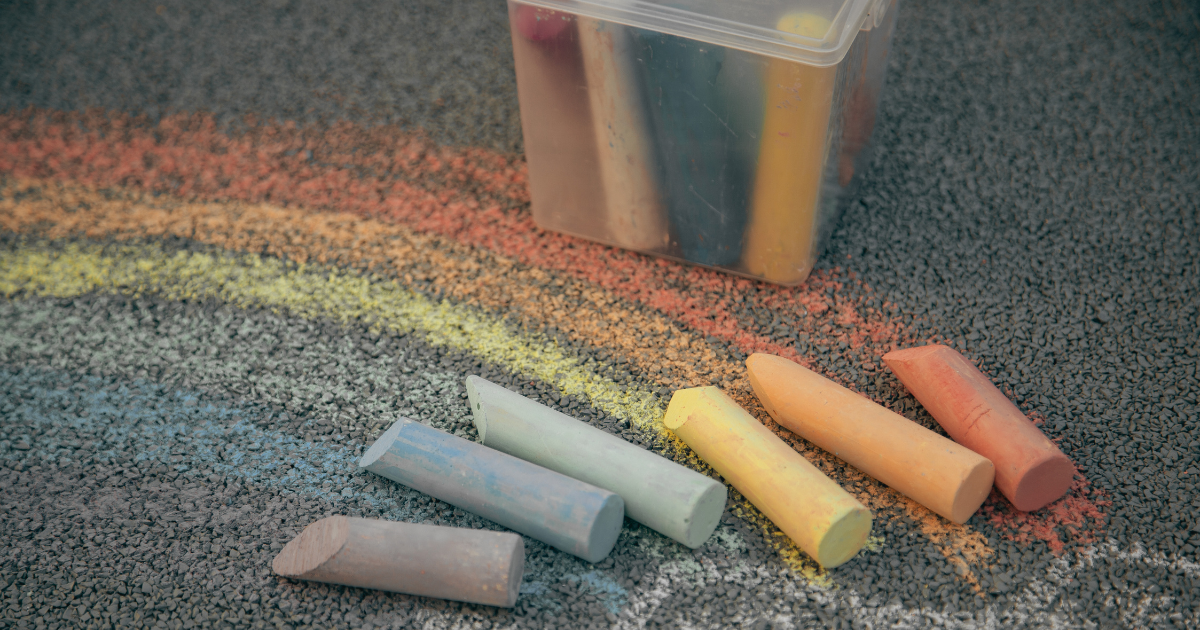 Colorful chalk pieces on a textured surface with chalk dust and a transparent container in the background