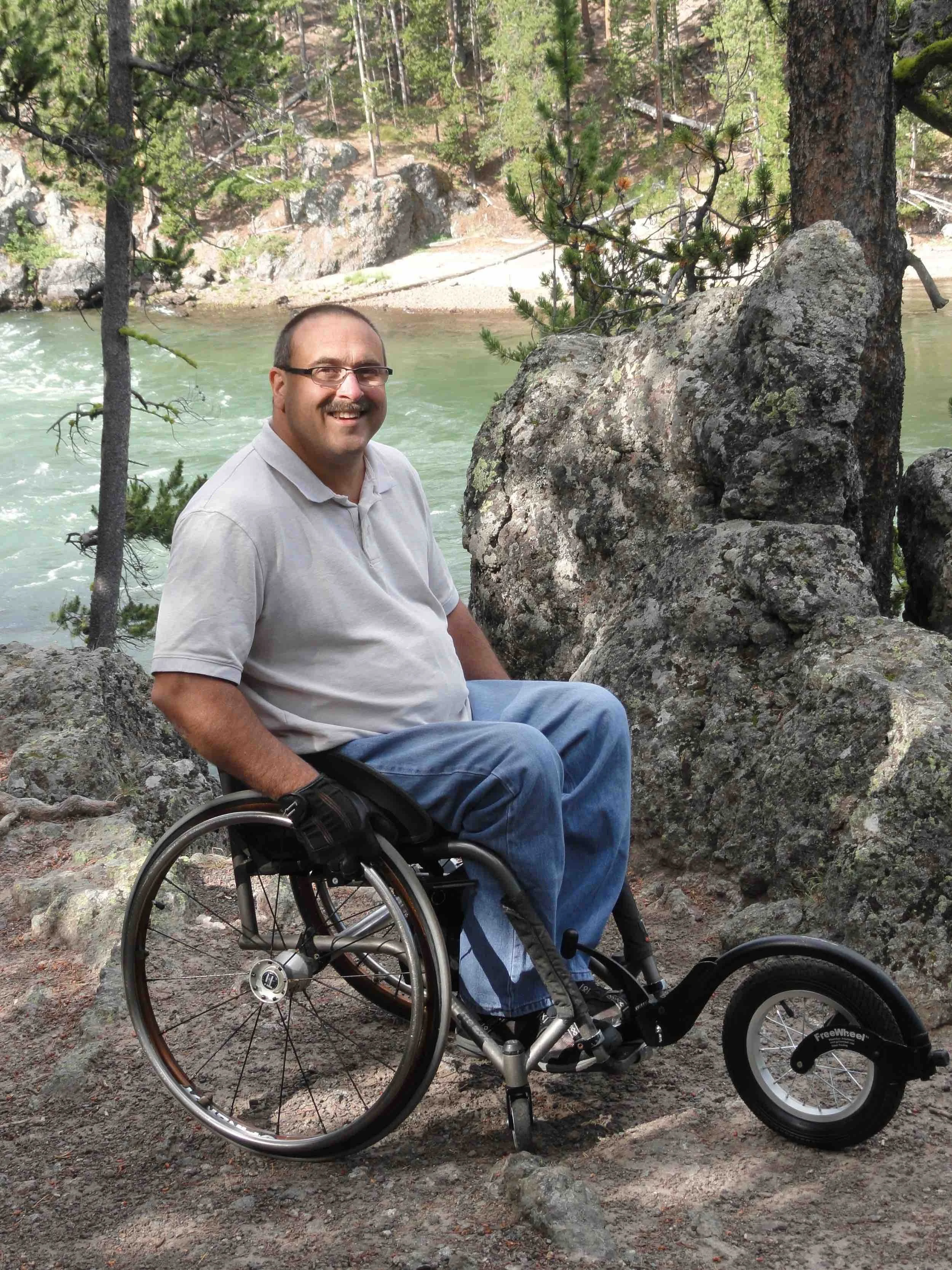 Mike Shultz enjoys a scenic lakeside overlook while seated in his wheelchair during a family travel adventure.