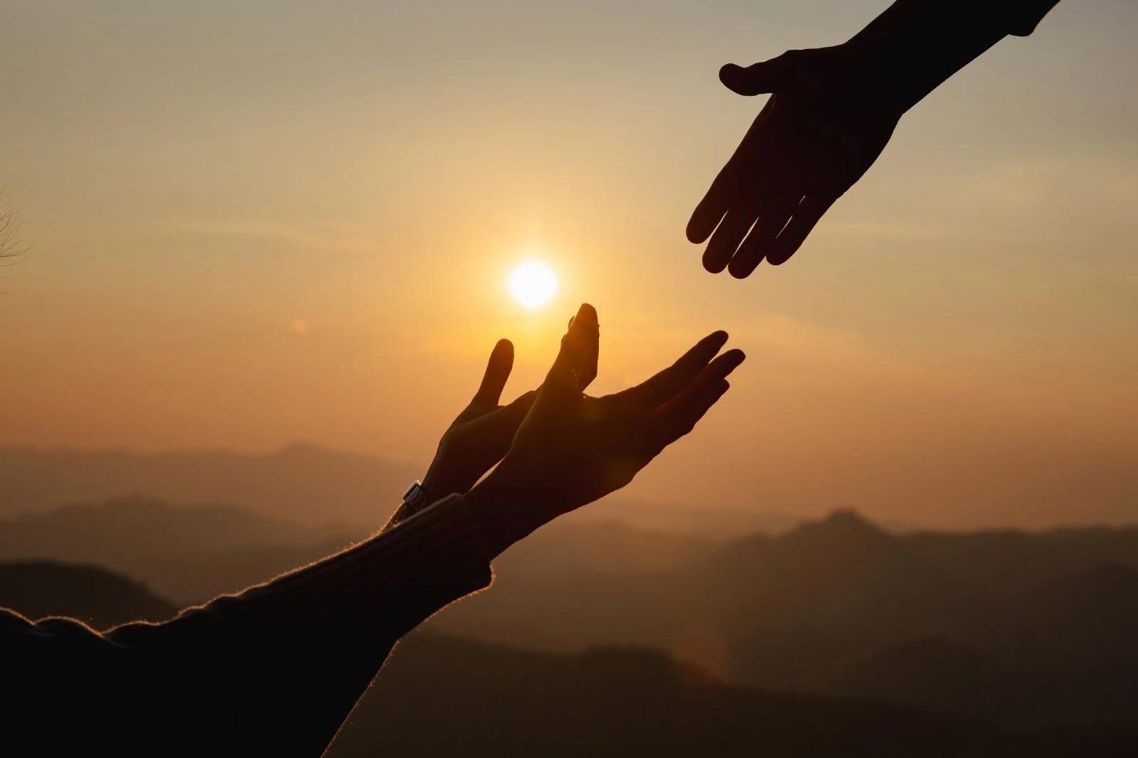 Silhouetted hands reaching toward one another at sunset, symbolizing hope, compassion, redemption, and the message of Mike Shultz's book You Can't Stop Love.