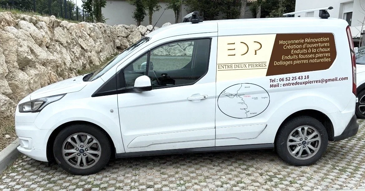 Véhicule utilitaire blanc avec publicité sur le côté pour une entreprise de maçonnerie, rénovation, création d'ouvertures, enduits à la chaux, fausses pierres et dallages naturels, avec coordonnées de contact.