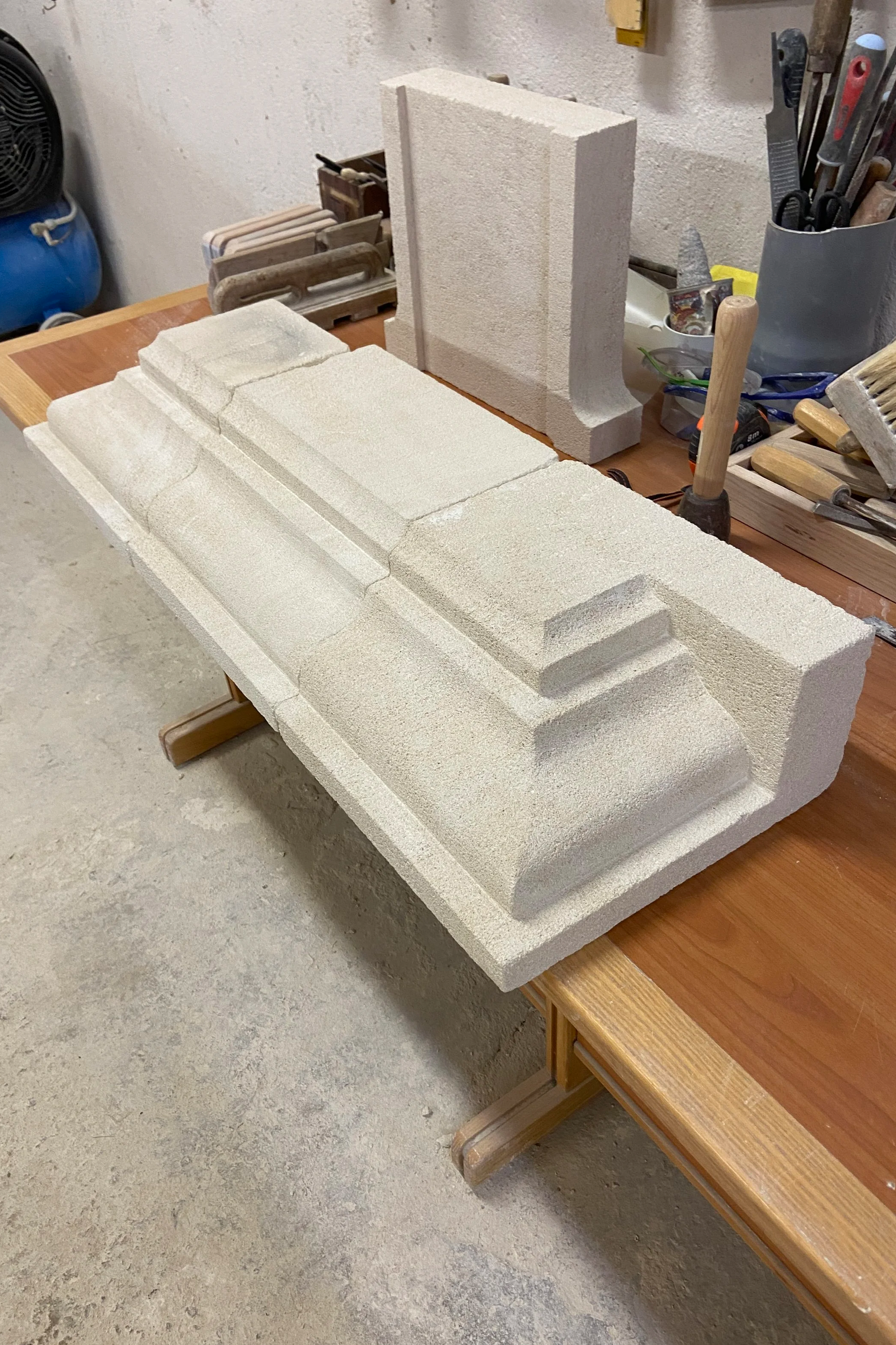 Table de travail avec des blocs de polystyrène pour une sculpture ou un projet de construction, outils tels que marteau, pince, escabeau, andriani, brosses, et autres outils de bricolage.