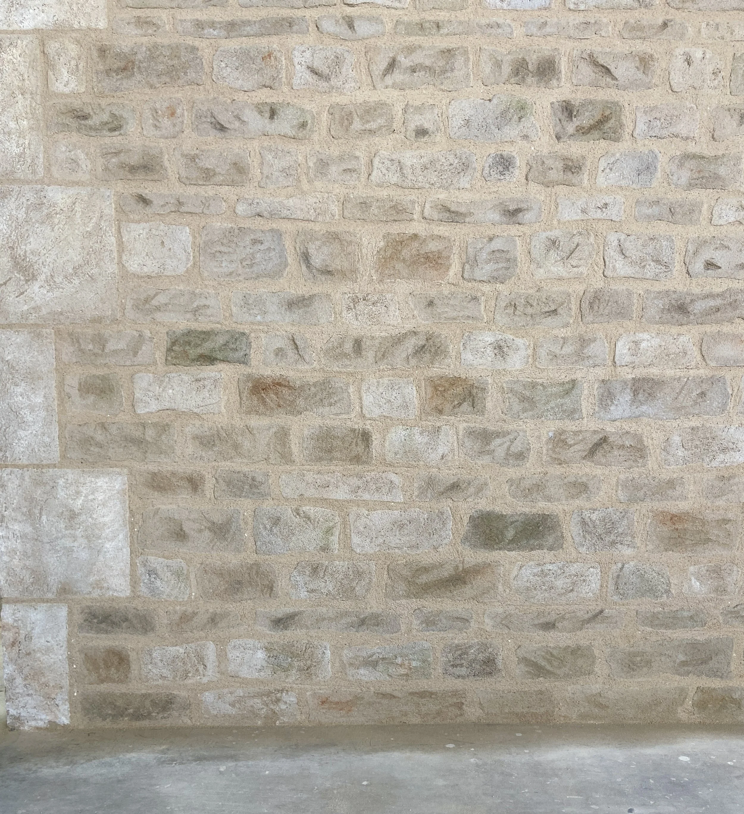 Mur en pierre beige avec des pierres de tailles et couleurs différentes, some motifs ethniques gravés sur la partie inférieure.
