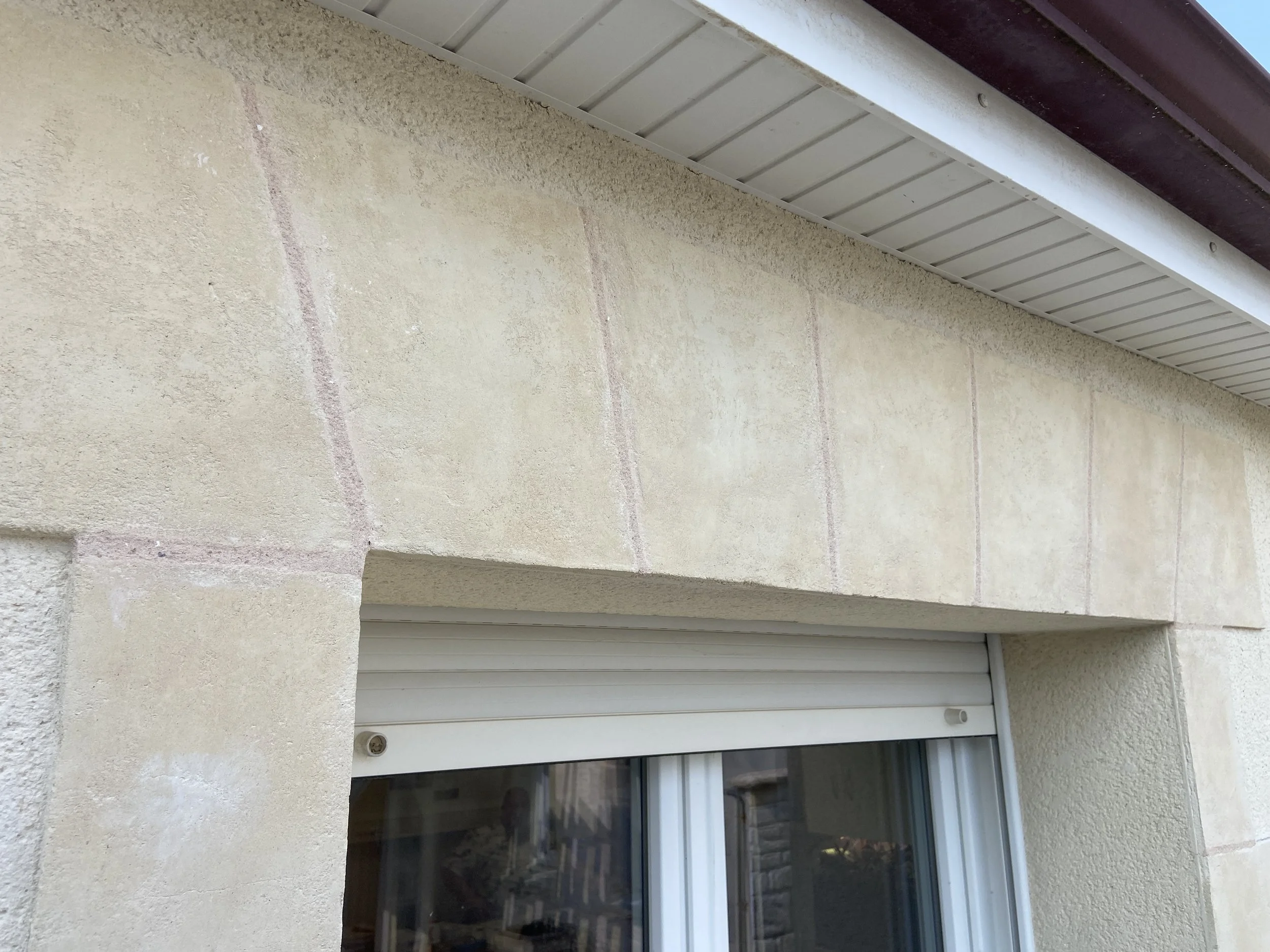 Facade de bâtiment avec mur en béton beige, fenêtre à volets roulants en partie inférieure, bardage en acier au plafond.