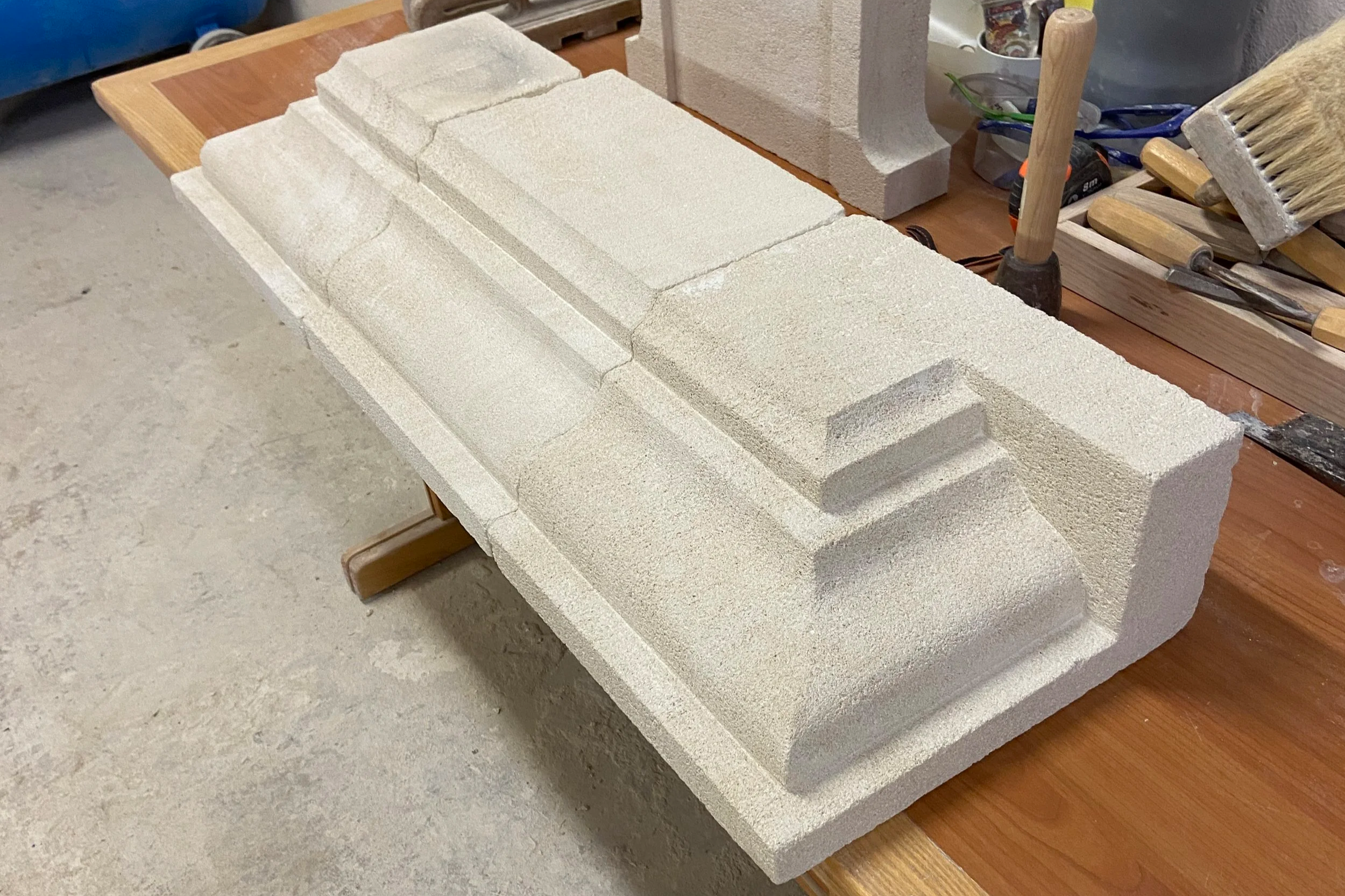 Des blocs de polystyrène blanc découpés pour la construction, posés sur une table en bois, avec des outils et matériaux de sculpture à proximité.