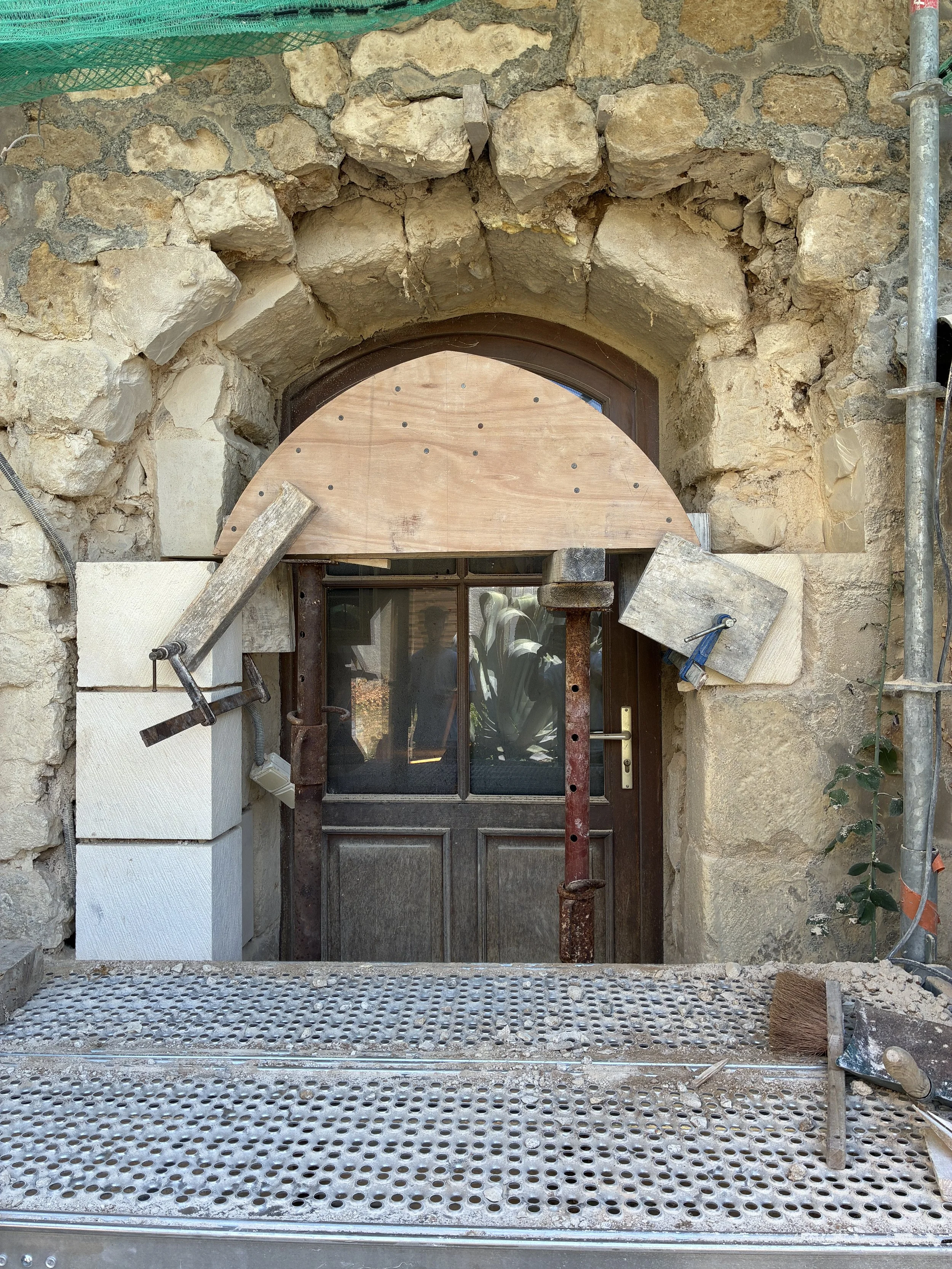 Travaux de restauration d'une porte ancienne avec un cadre en bois et une arche de pierre, assumant un chantier de rénovation.