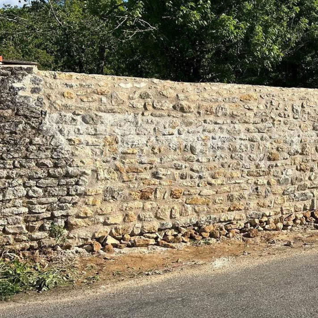 Un mur en pierre le long d'une route avec des arbres en arrière-plan.