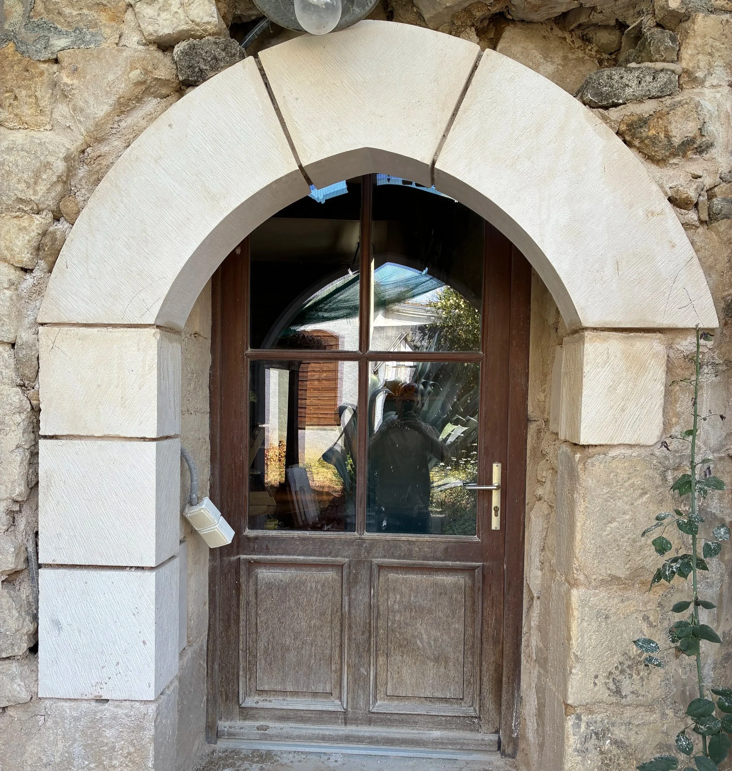 Une porte en bois avec une fenêtre en verre divisée en quatre parties, encadrée par un arc en pierre.
