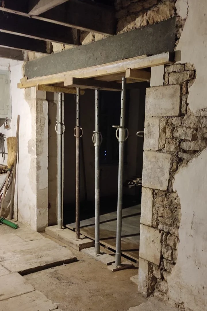 Travaux de rénovation avec des échafaudages en métal devant une ouverture dans un mur en pierre.