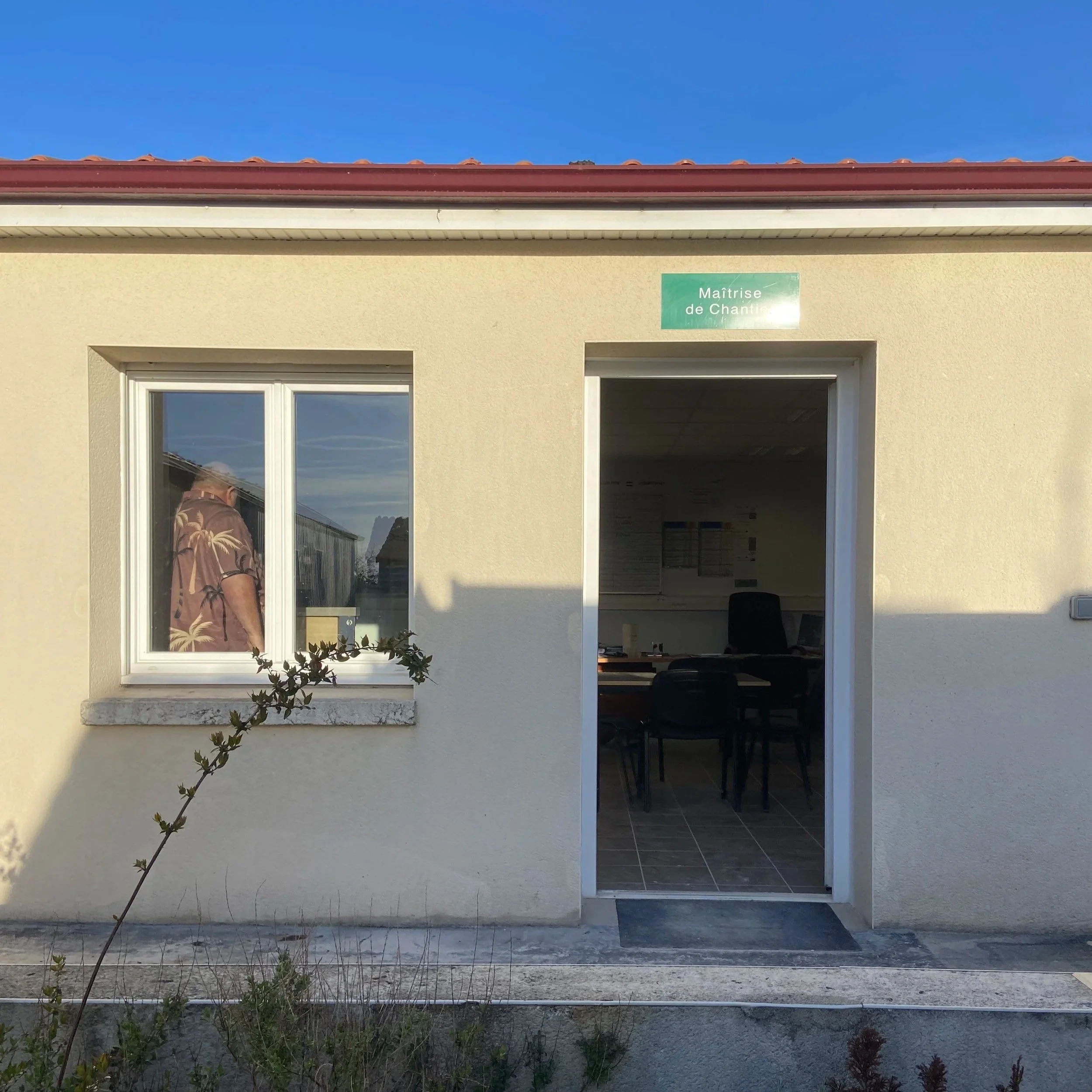 Façade d'une maison avec un portail blanc, une fenêtre et une plaque verte avec l'inscription 'Maîtrise de Chantier'.