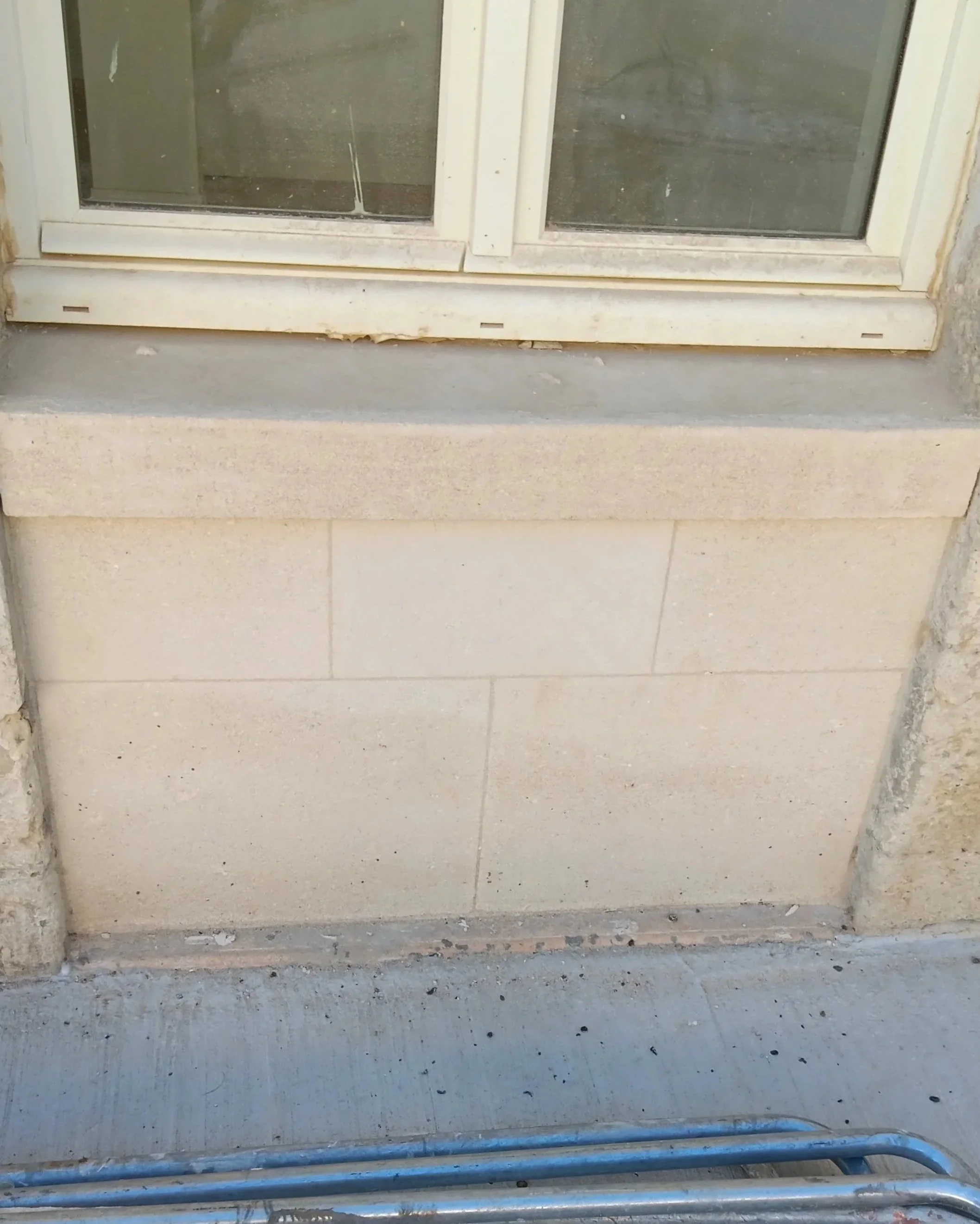 Vue d'une porte en verre dans un cadre blanc, avec un seuil et un mur en béton en dessous, et des tuyaux en métal à l'avant.