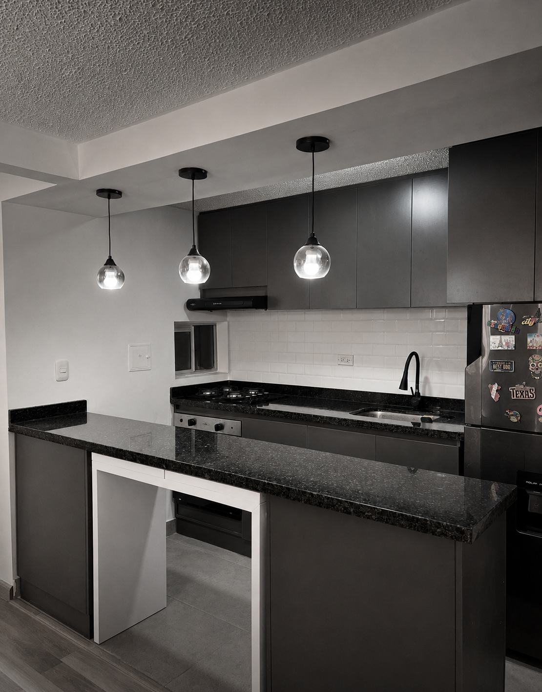 Modern kitchen with black countertops, gray cabinets, white subway tile backsplash, and pendant lighting.
