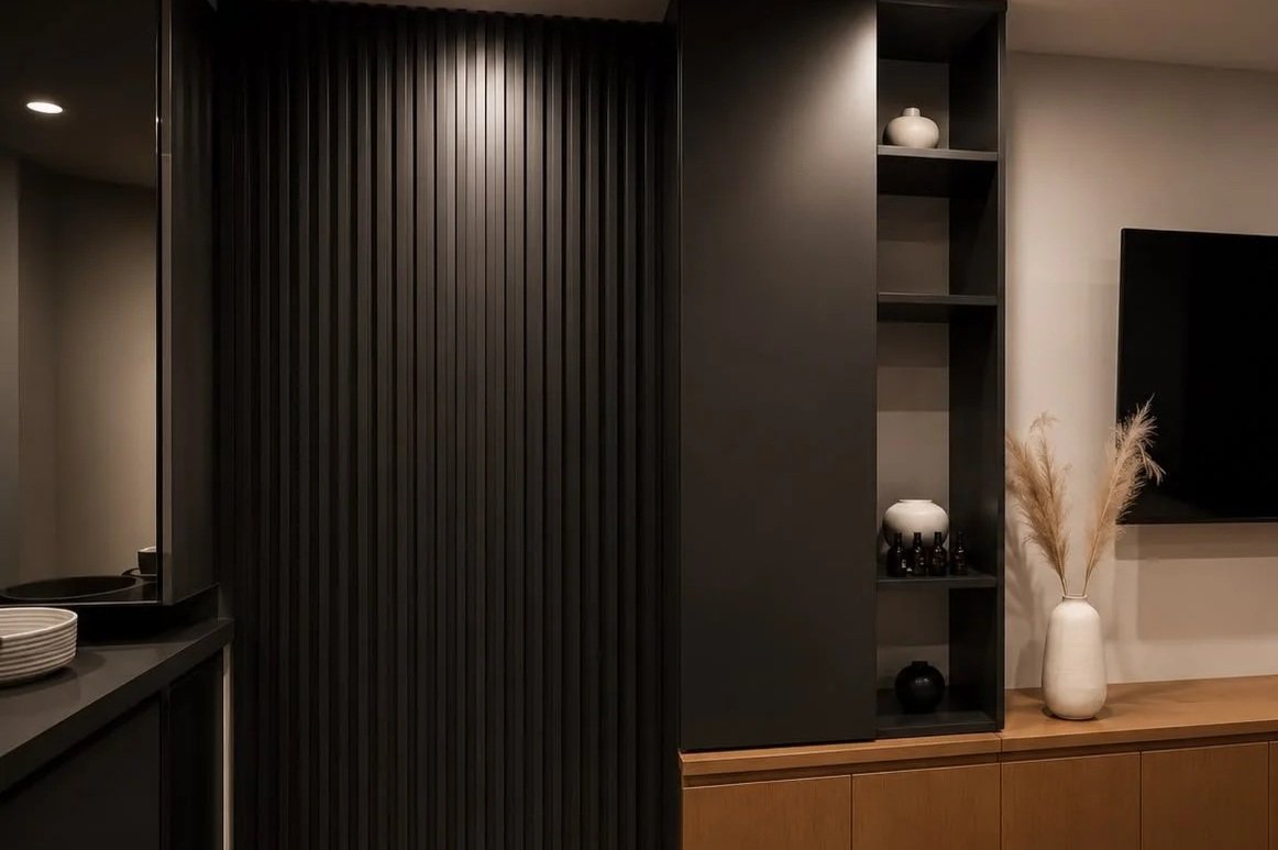 Interior living room with dark wood paneling, a built-in black shelving unit with vases and decorative objects, and a white vase with dried grasses.