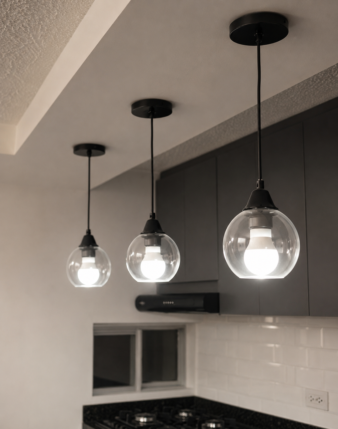 Three modern hanging pendant lights with glass globes illuminate a kitchen ceiling.