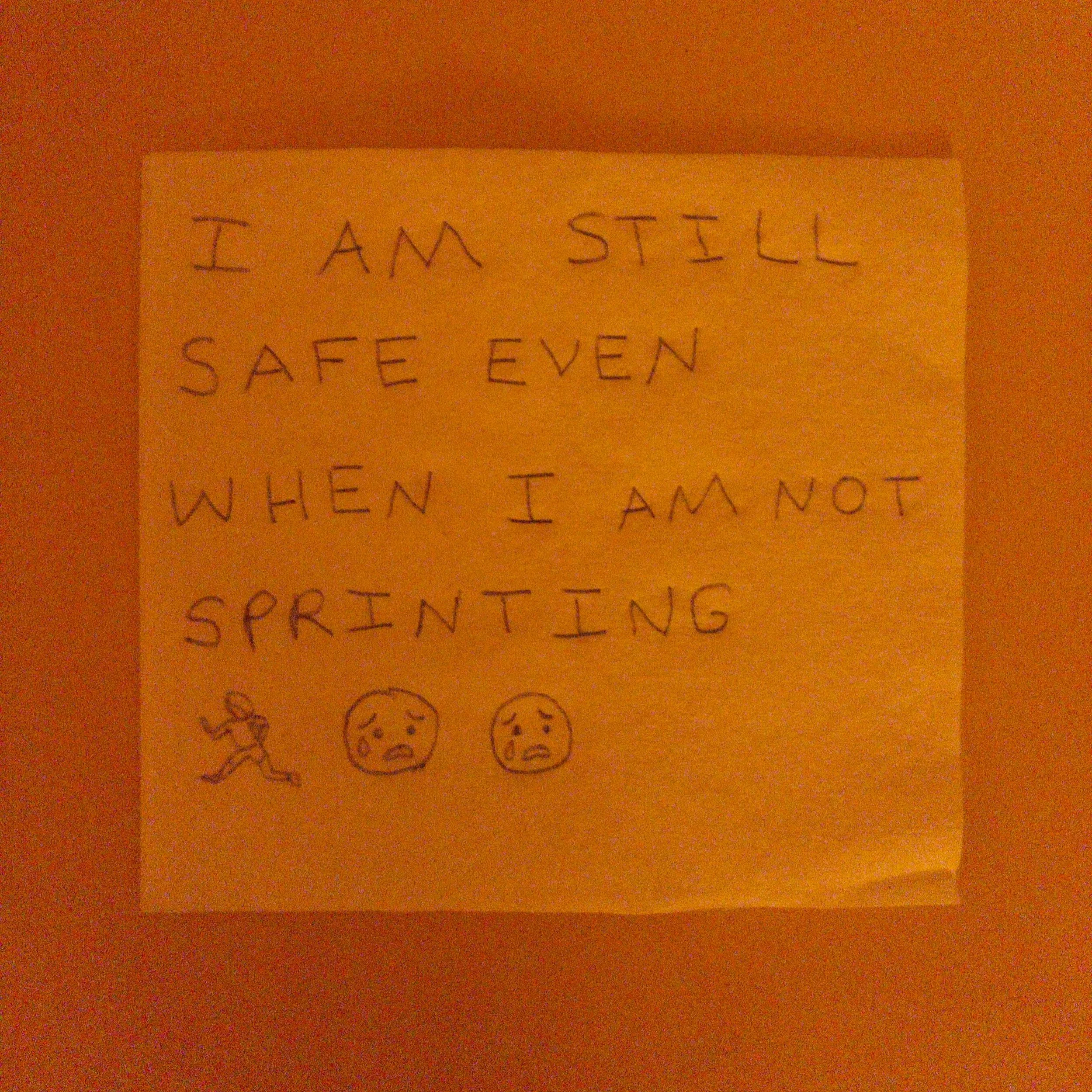 Handwritten note on orange paper reads 'I AM STILL SAFE EVEN WHEN I AM NOT SPRINTING' with simple emoticon faces underneath.