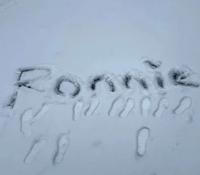 'Ronnie' written in snow with footprints around it.